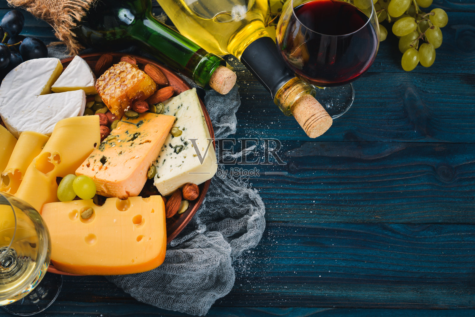 蓝色的木桌上放着各式各样的奶酪、葡萄酒、蜂蜜、坚果和香料。前视图。文本的空闲空间。照片摄影图片