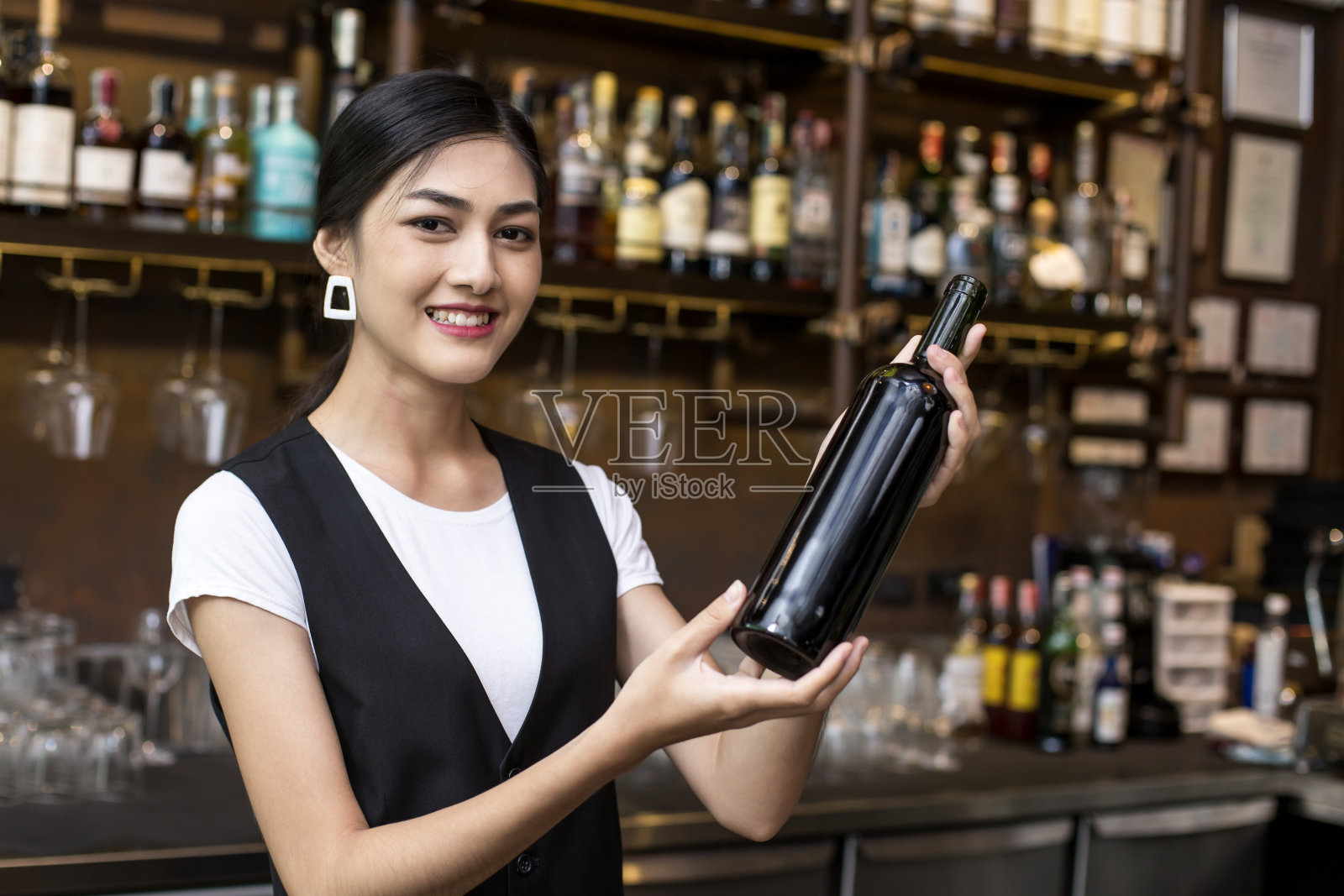 年轻亚洲女性服务员餐厅餐饮服务快乐情感。女服务员在酒吧为顾客端红酒。在酒吧概念的女人与葡萄酒。照片摄影图片
