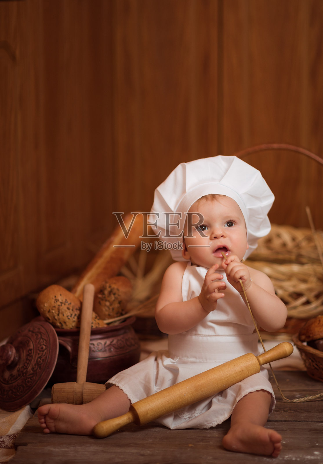 一个小男孩穿着厨师服装，坐在棕色的木地板上烤着面包和糖果照片摄影图片