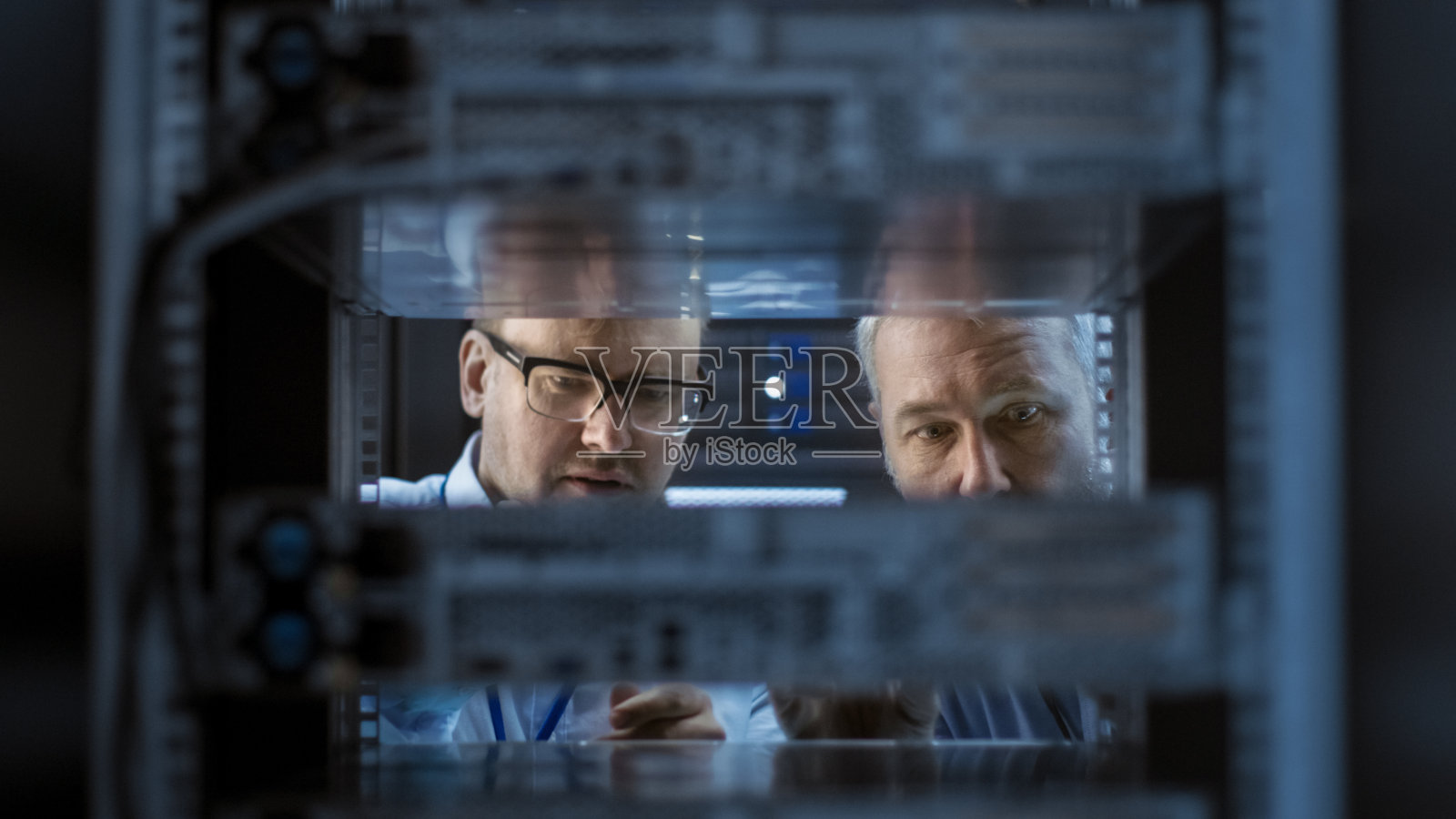 2名服务器工程师在服务器机架安装硬件。他们在大型现代数据中心工作。照片摄影图片