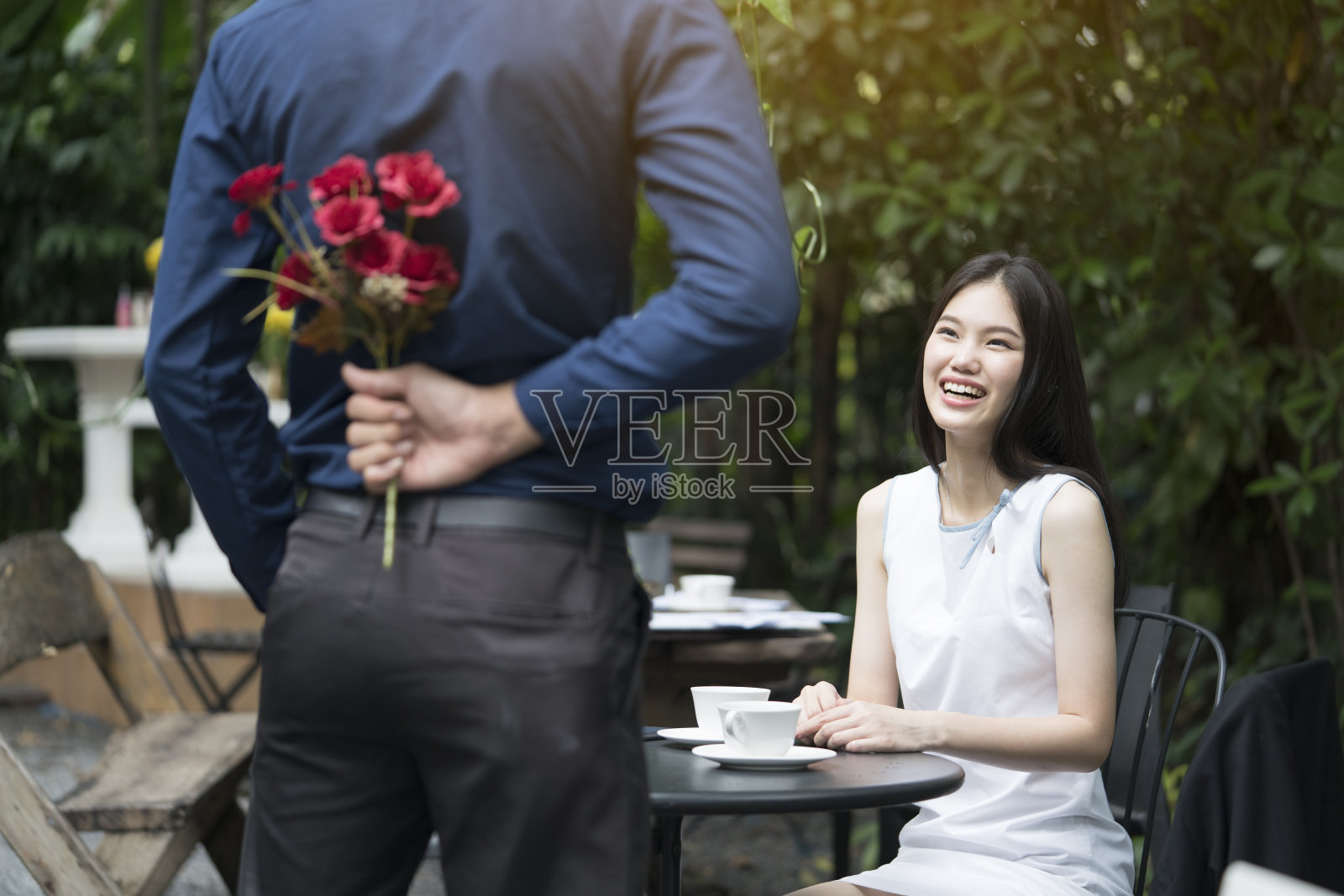 一个男人在美丽的花园中捧着一束可爱的鲜花向一个微笑的女人求婚，情人和情侣的概念，令人惊讶的求婚照片摄影图片
