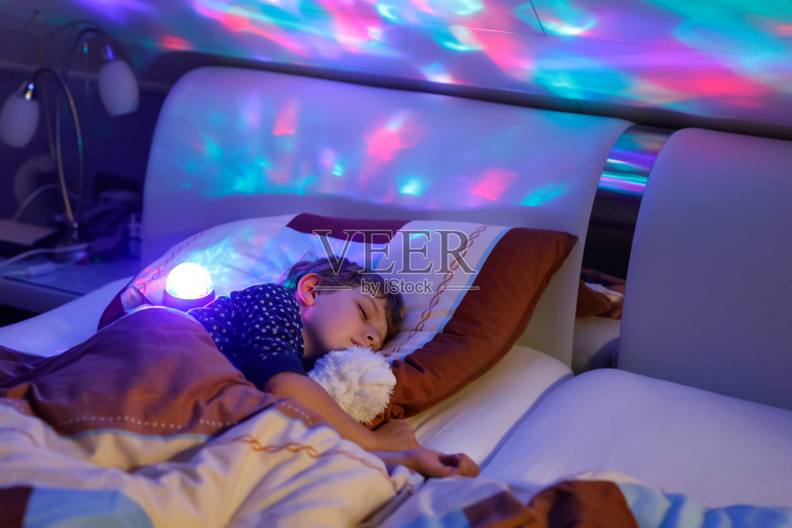 学龄前的小男孩睡在五颜六色的台灯下。照片摄影图片