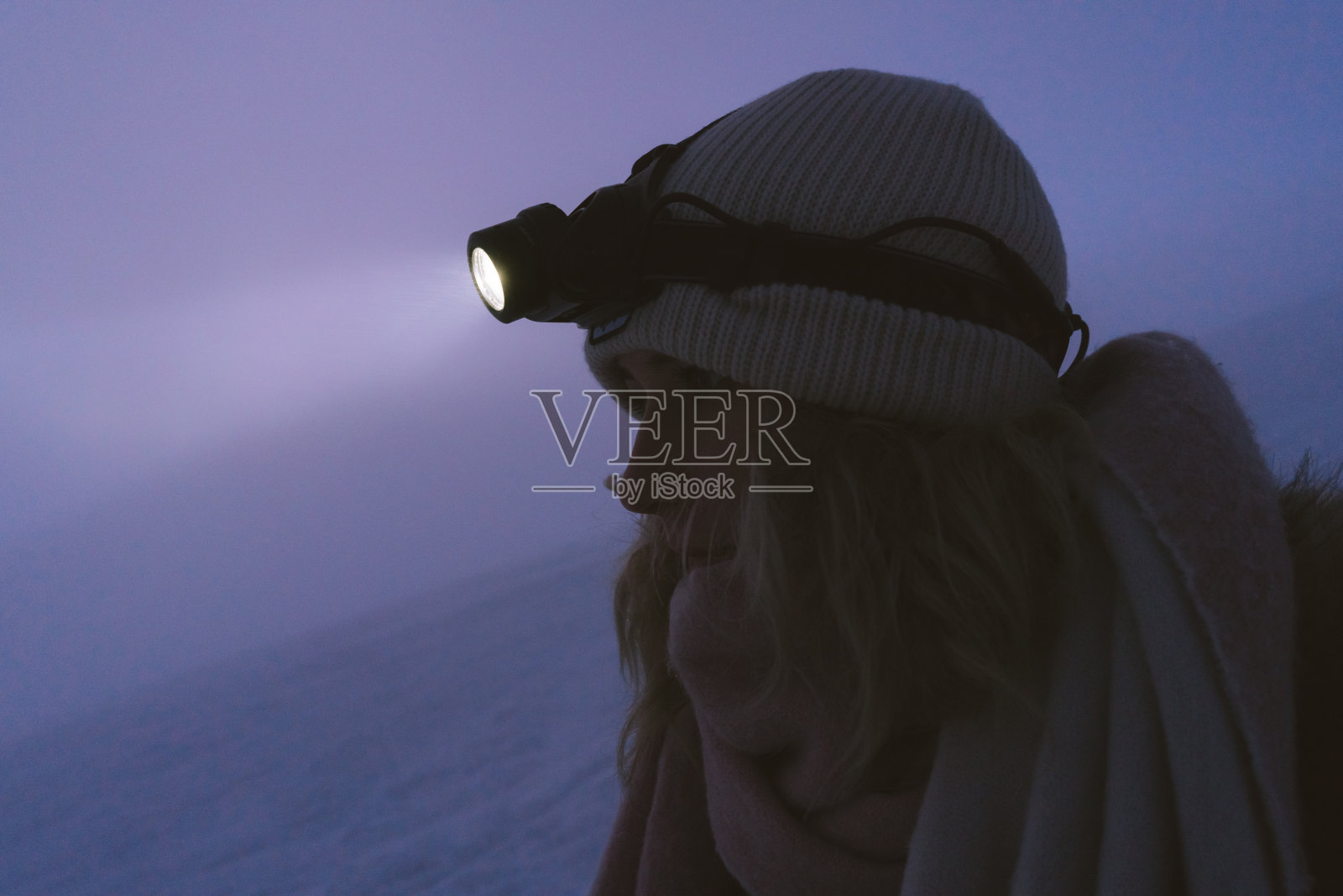 在冬季日落后，在斯洛伐克山脉上的雪上带着头灯的徒步妇女照片摄影图片