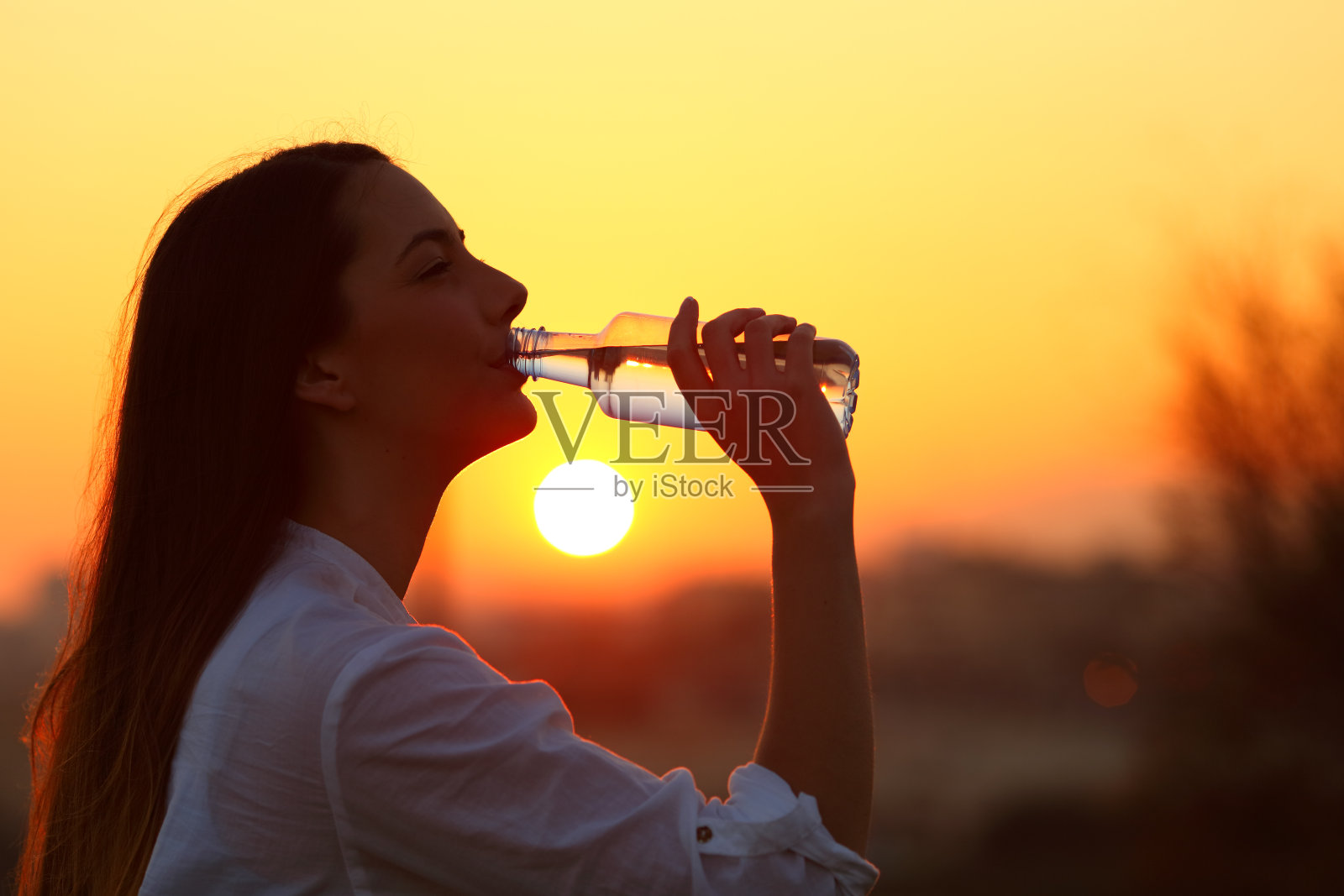 一个女人从瓶子里喝水的背光照片摄影图片