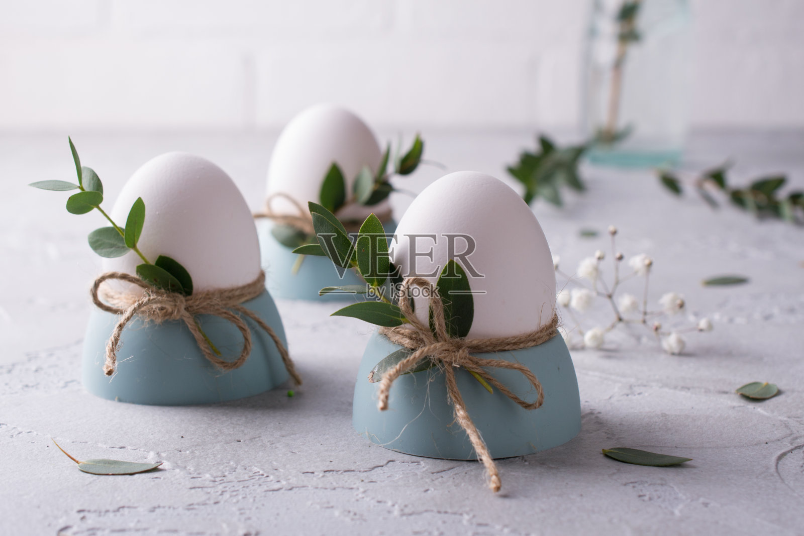 复活节餐桌上摆放着白色的鸡蛋，在蛋杯，桉树的叶枝上。在灰色的混凝土背景上。照片摄影图片