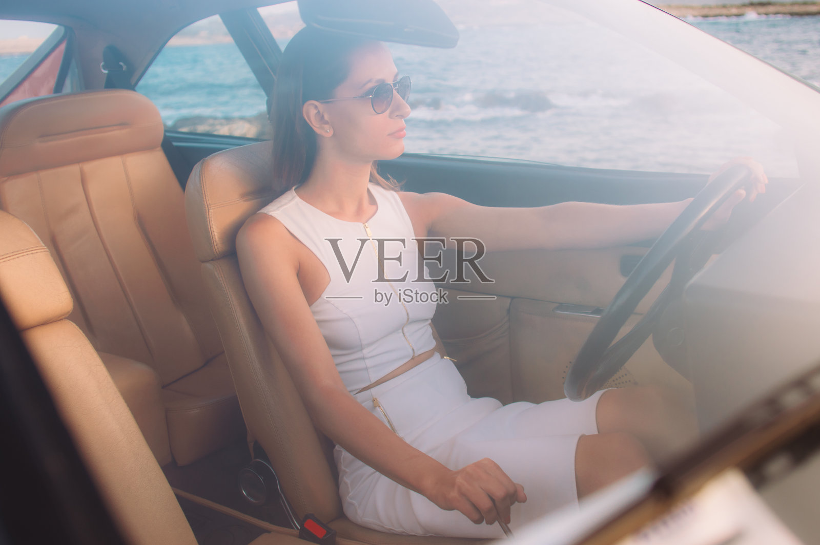 穿着白色连衣裙的年轻女孩坐在汽车的前座上照片摄影图片
