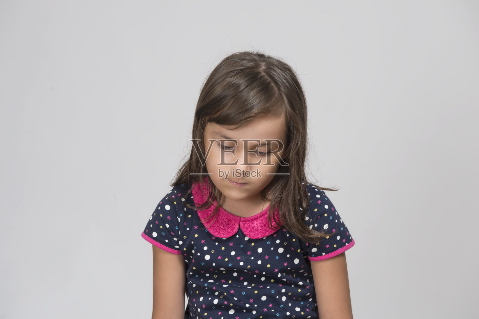 一个在灰色背景下向下看的悲伤的孩子的肖像照片摄影图片