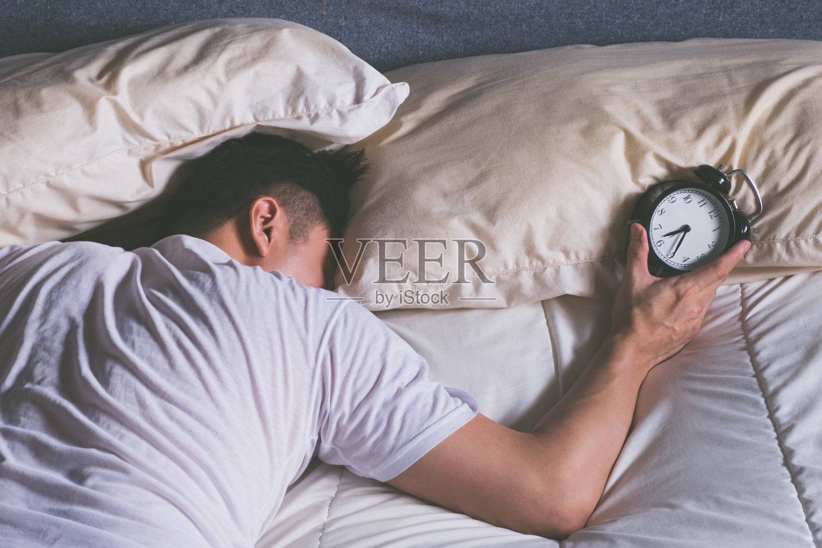 正在睡觉的亚洲年轻男子清晨被闹钟吵醒照片摄影图片