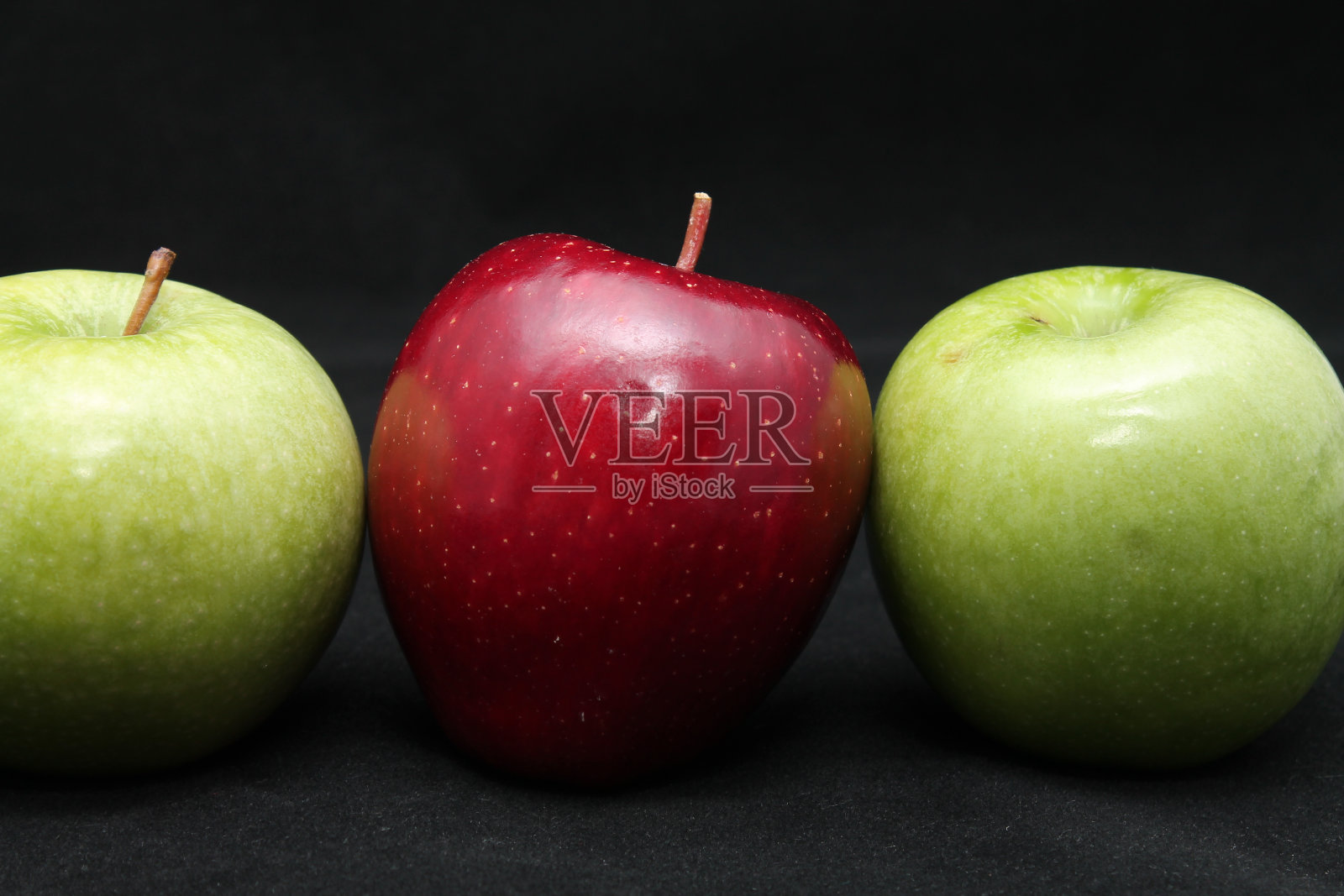 三个绿色和红色的苹果在黑色的背景上排成一排的特写照片摄影图片