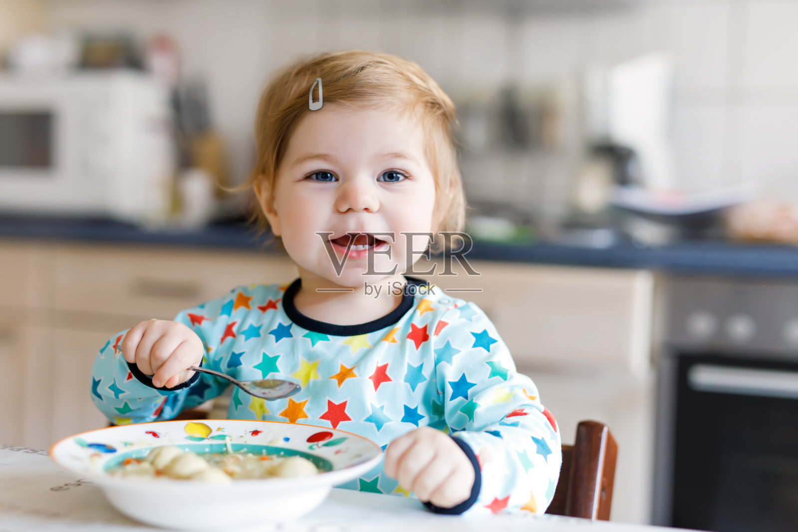 可爱的小女孩用勺子吃蔬菜面汤。食品、儿童、喂养和人的概念照片摄影图片