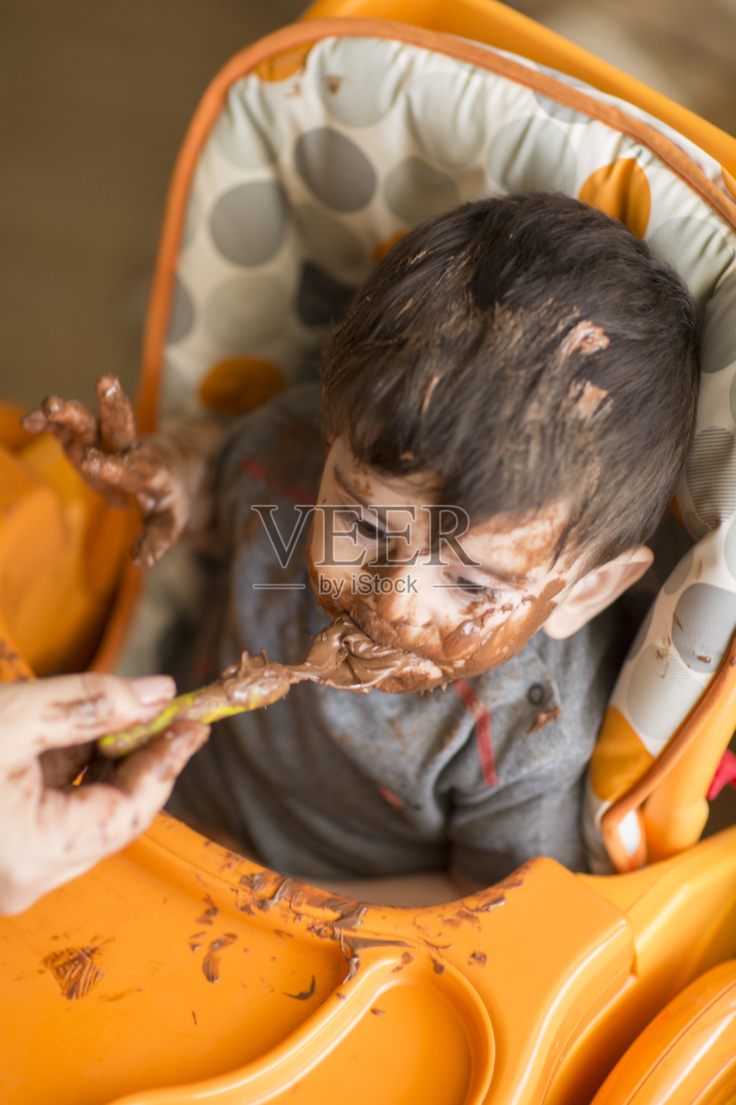 高脚椅上的小男孩，吃着巧克力照片摄影图片