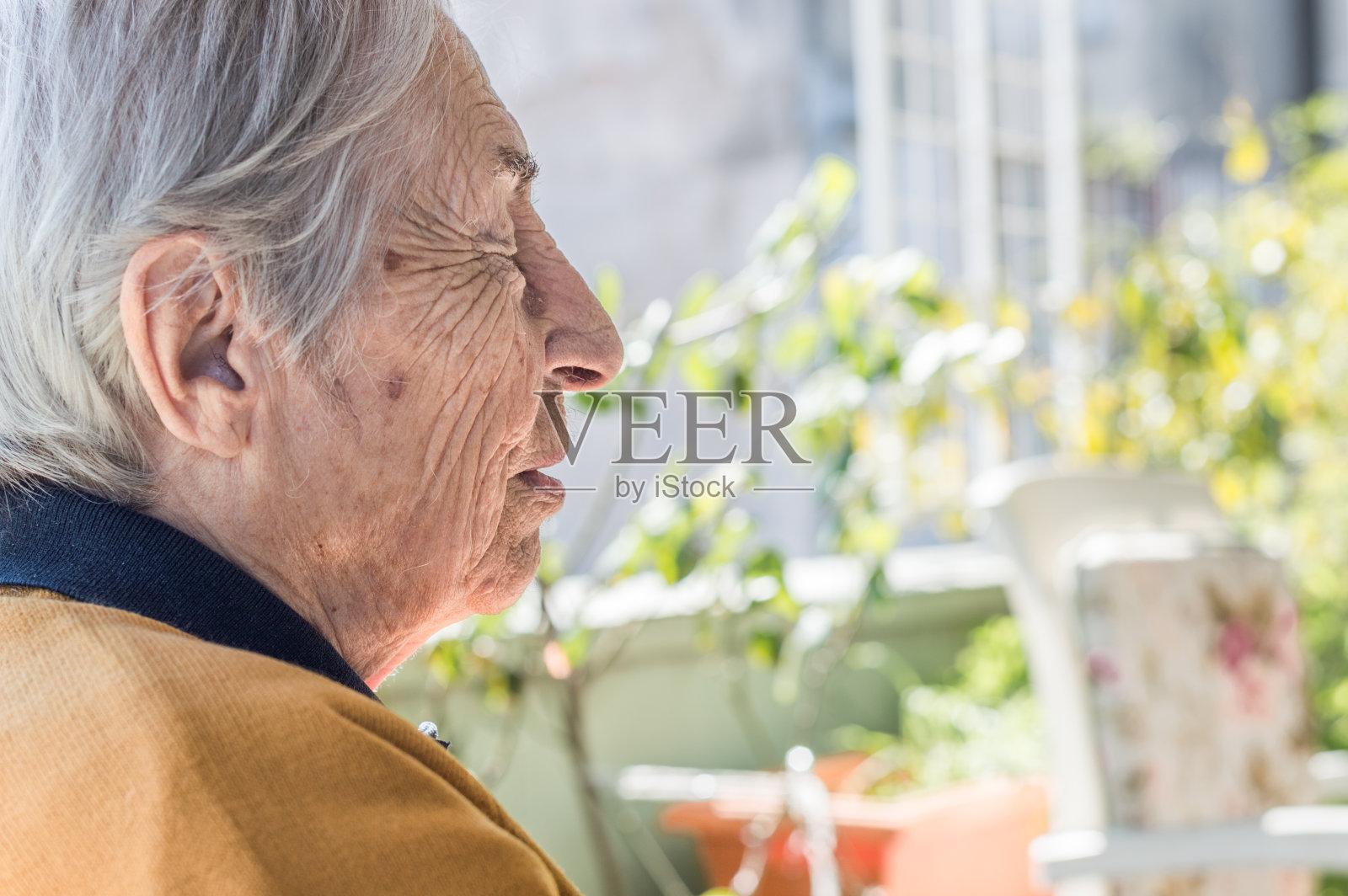 在一个阳光明媚的日子里，一位老妇人坐在阳台上休息。照片摄影图片