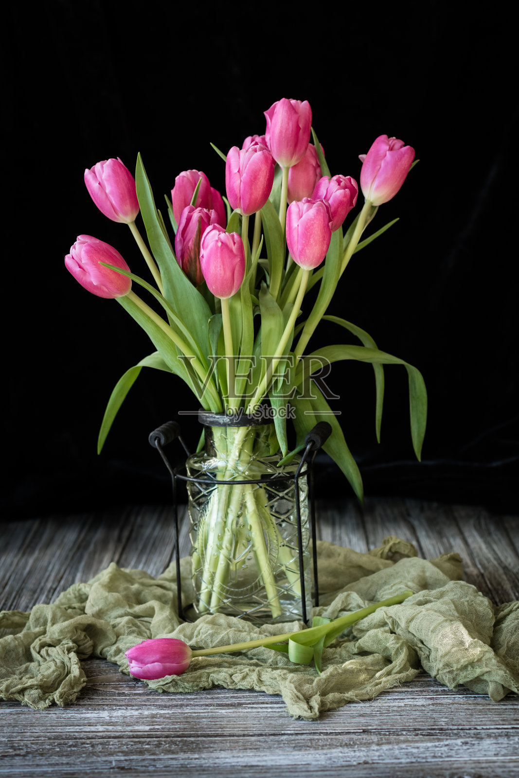 一束明亮的洋红色郁金香放在玻璃丝花瓶里。照片摄影图片