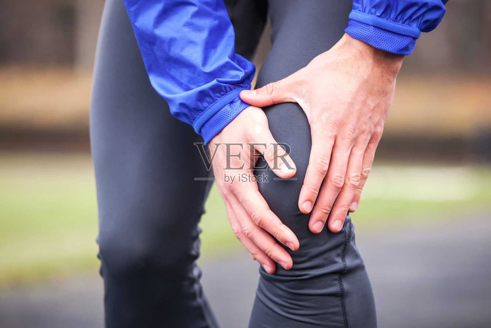 一个年轻的跑步者在跑步时抱着他受伤的膝盖。照片摄影图片