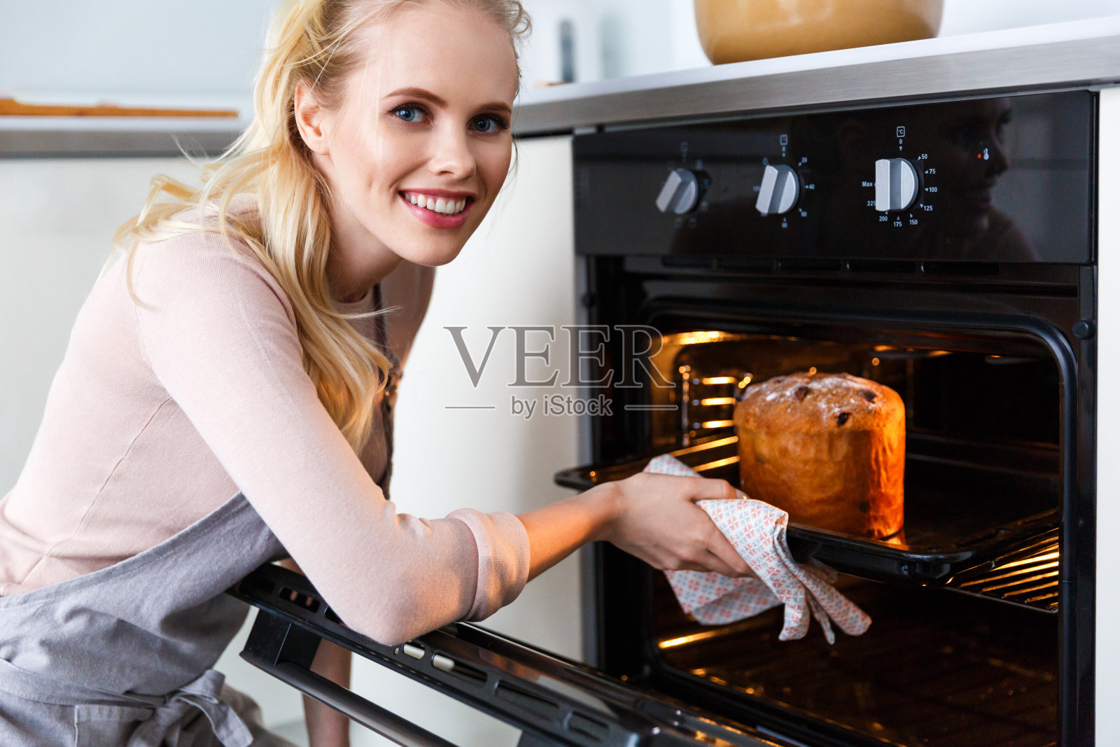 穿着围裙的漂亮年轻女子在烤箱里烤复活节蛋糕，对着镜头微笑照片摄影图片
