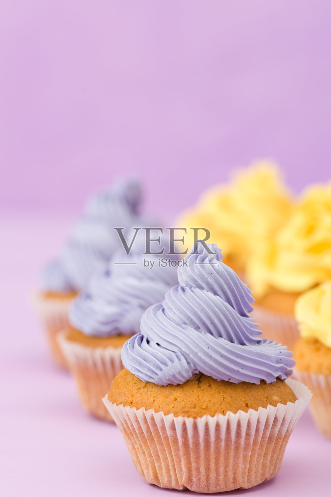 纸杯蛋糕装饰与黄色奶油在紫罗兰粉背景贺卡与copyscape。照片摄影图片