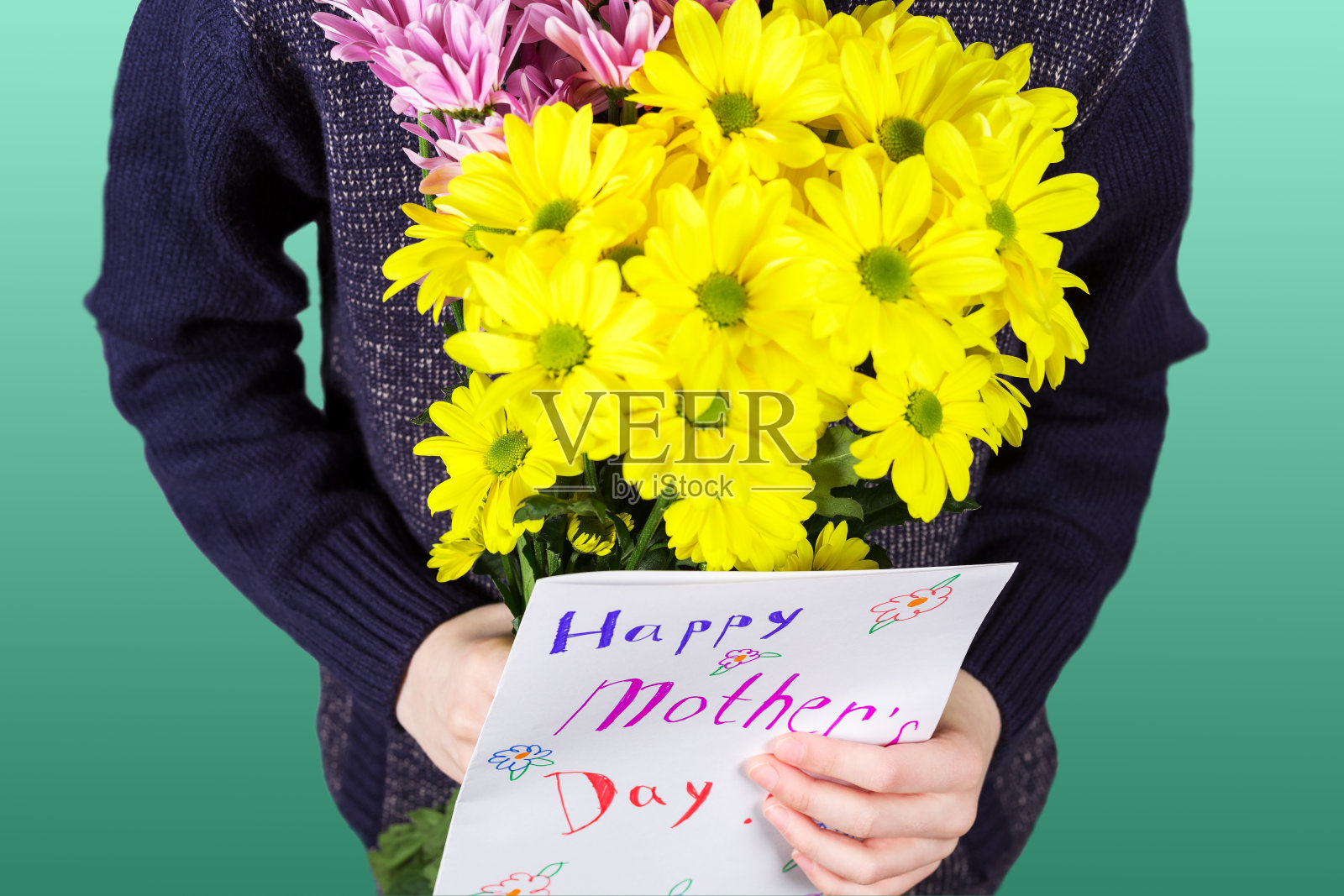 男孩手里捧着一束黄色和粉红色的菊花和手工制作的贺卡“母亲节快乐”。给妈妈买花和礼物照片摄影图片