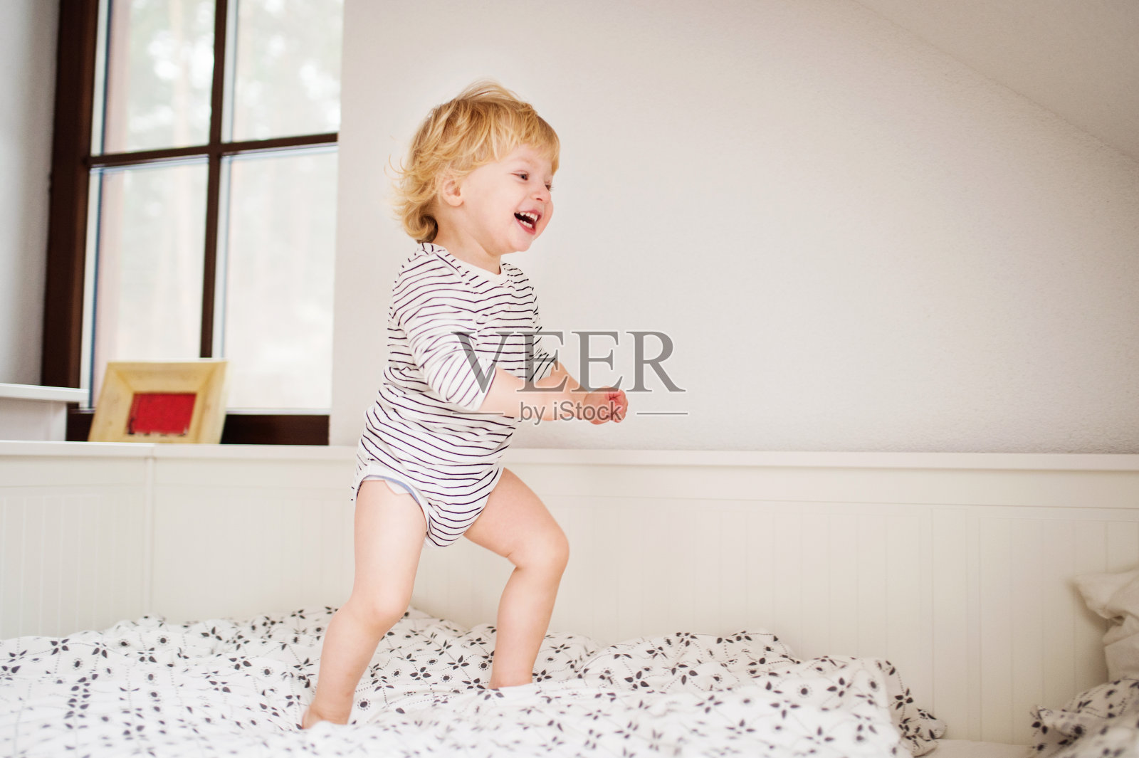 可爱的蹒跚学步的男孩在床上跳。照片摄影图片