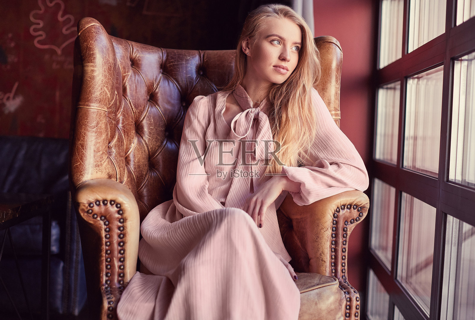 美丽优雅的金发女人穿着粉红色的衣服坐在皮革扶手椅上照片摄影图片