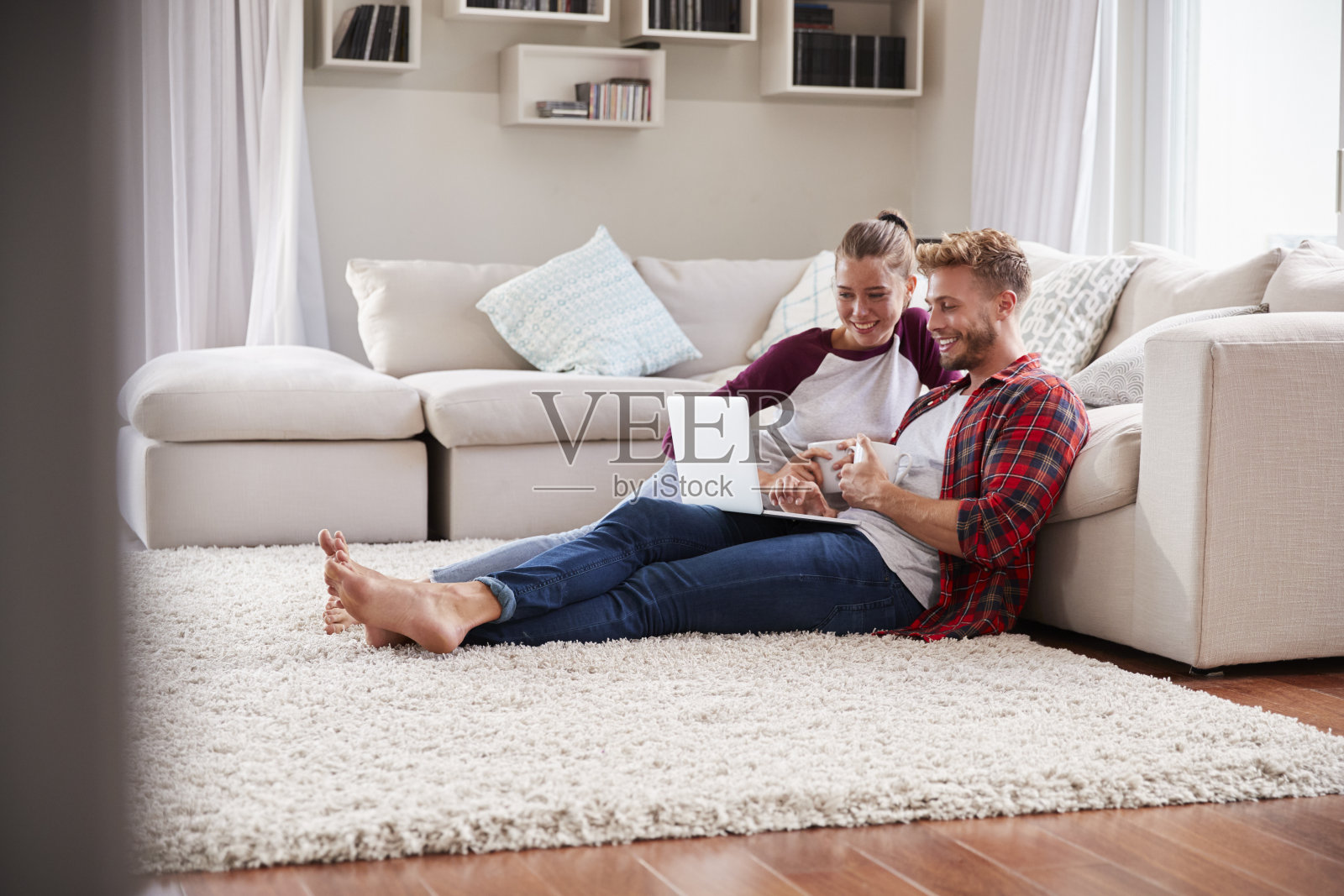 一对年轻的白人夫妇坐在家里的地板上用笔记本电脑照片摄影图片