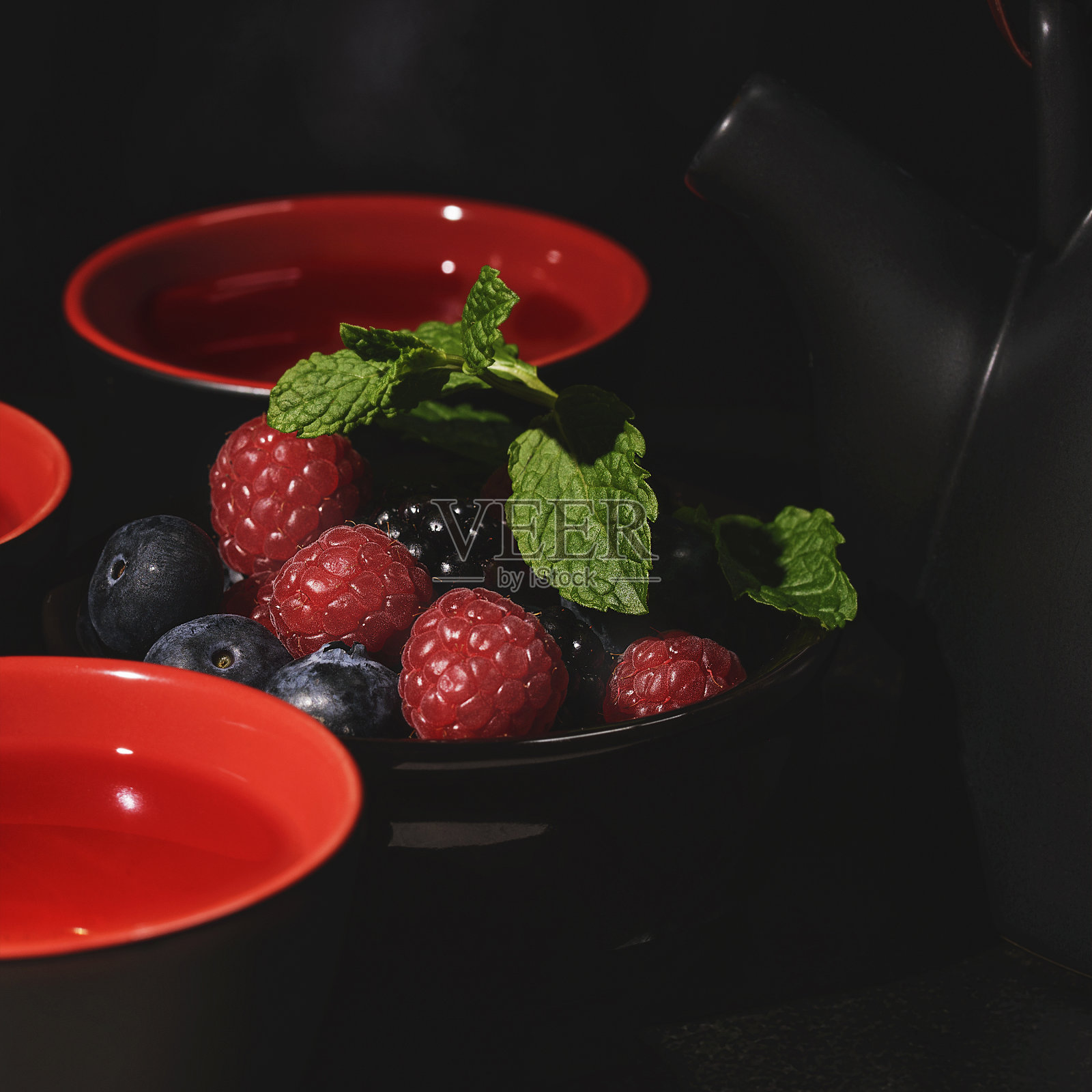 茶具摆放在桌子上，黑色和红色的杯子，上面有黑红色的浆果。照片摄影图片