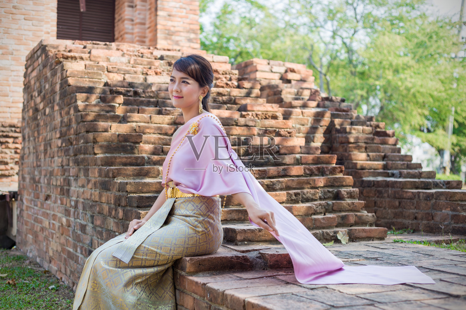 妇女坐在穿着泰国传统布料或泰国服装在古代城市和墙壁的背景。照片摄影图片