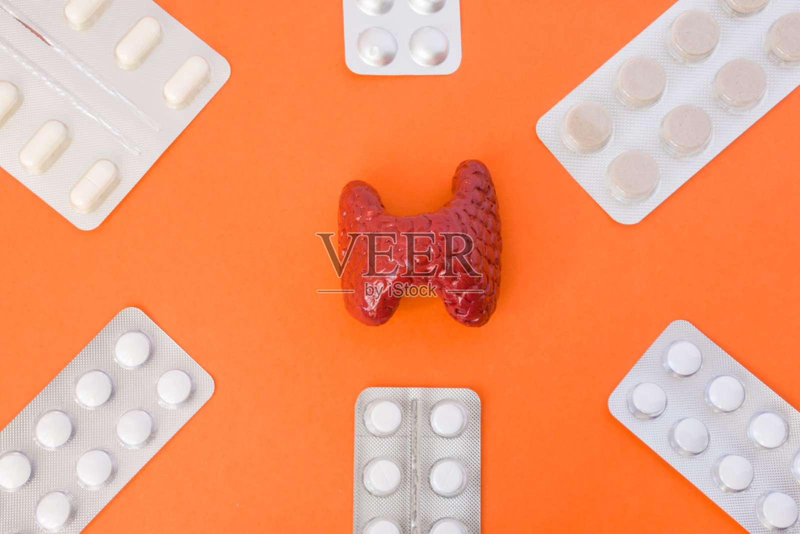 在橙色背景的图片中，一个被六个白色药丸包裹的甲状腺模型。照片概念艺术治疗或激素替代治疗的甲状腺照片摄影图片