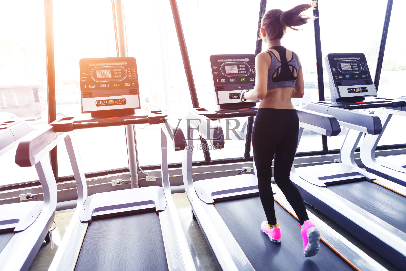 年轻的运动妇女在晨光升起时在健身房的电动跑步机上跑步。照片摄影图片