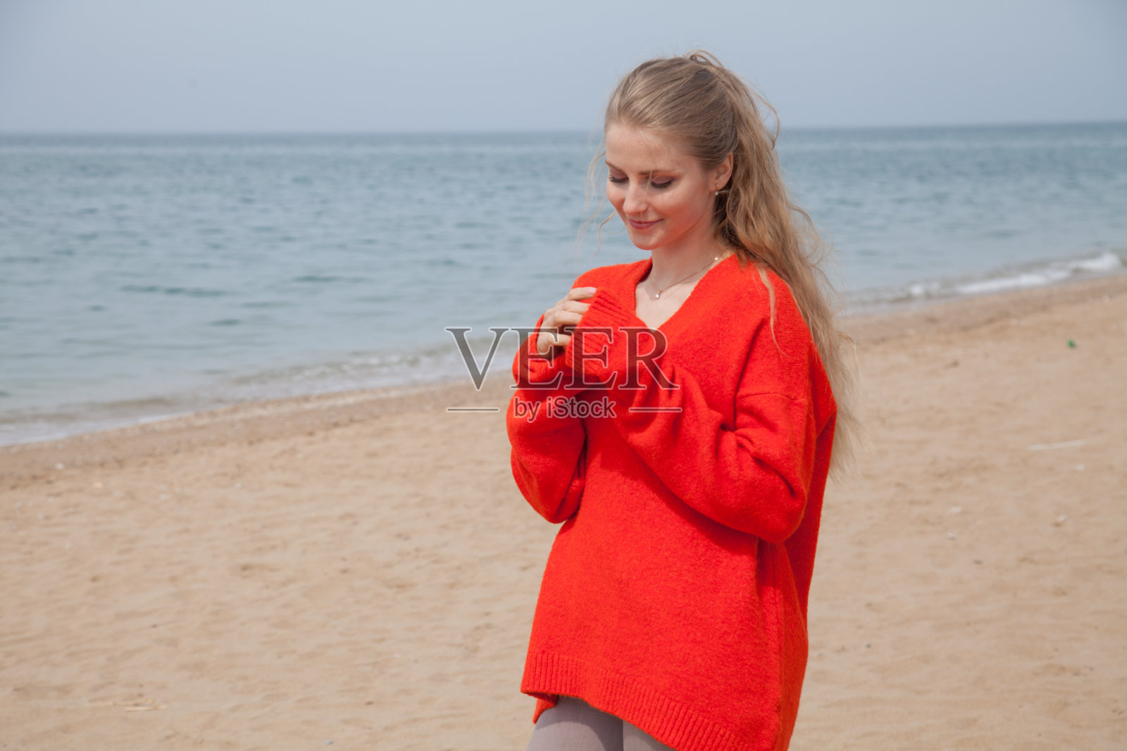 那个穿红衣服的金发女郎沿着海边的海滩散步照片摄影图片