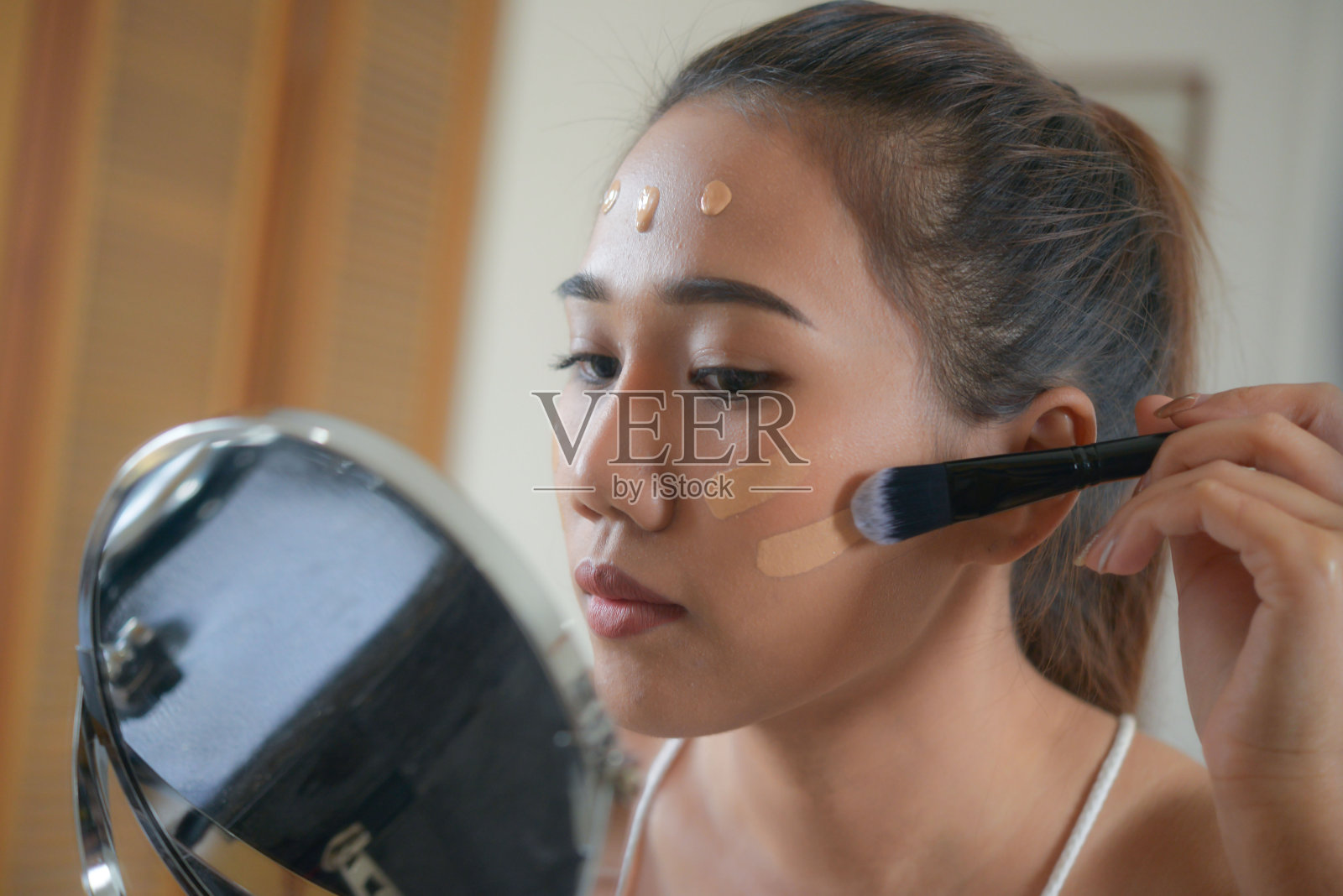 亚洲妇女在她的脸上为美丽涂抹粉底。照片摄影图片