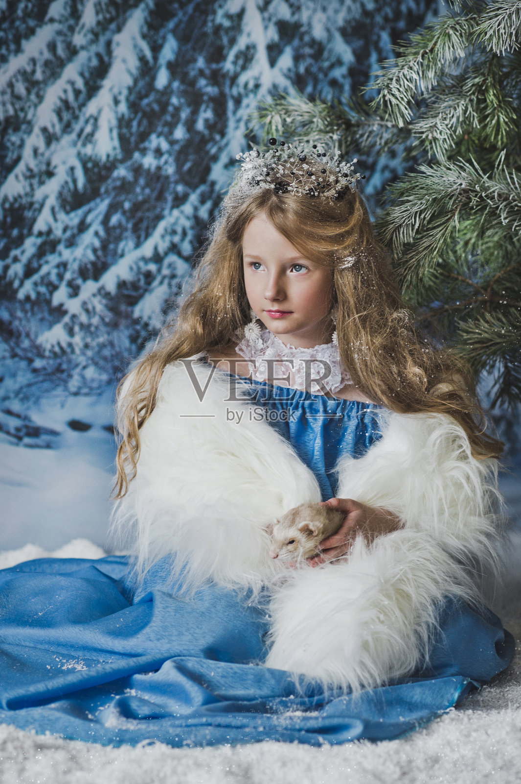 白雪公主坐在圣诞树前的雪地里。照片摄影图片