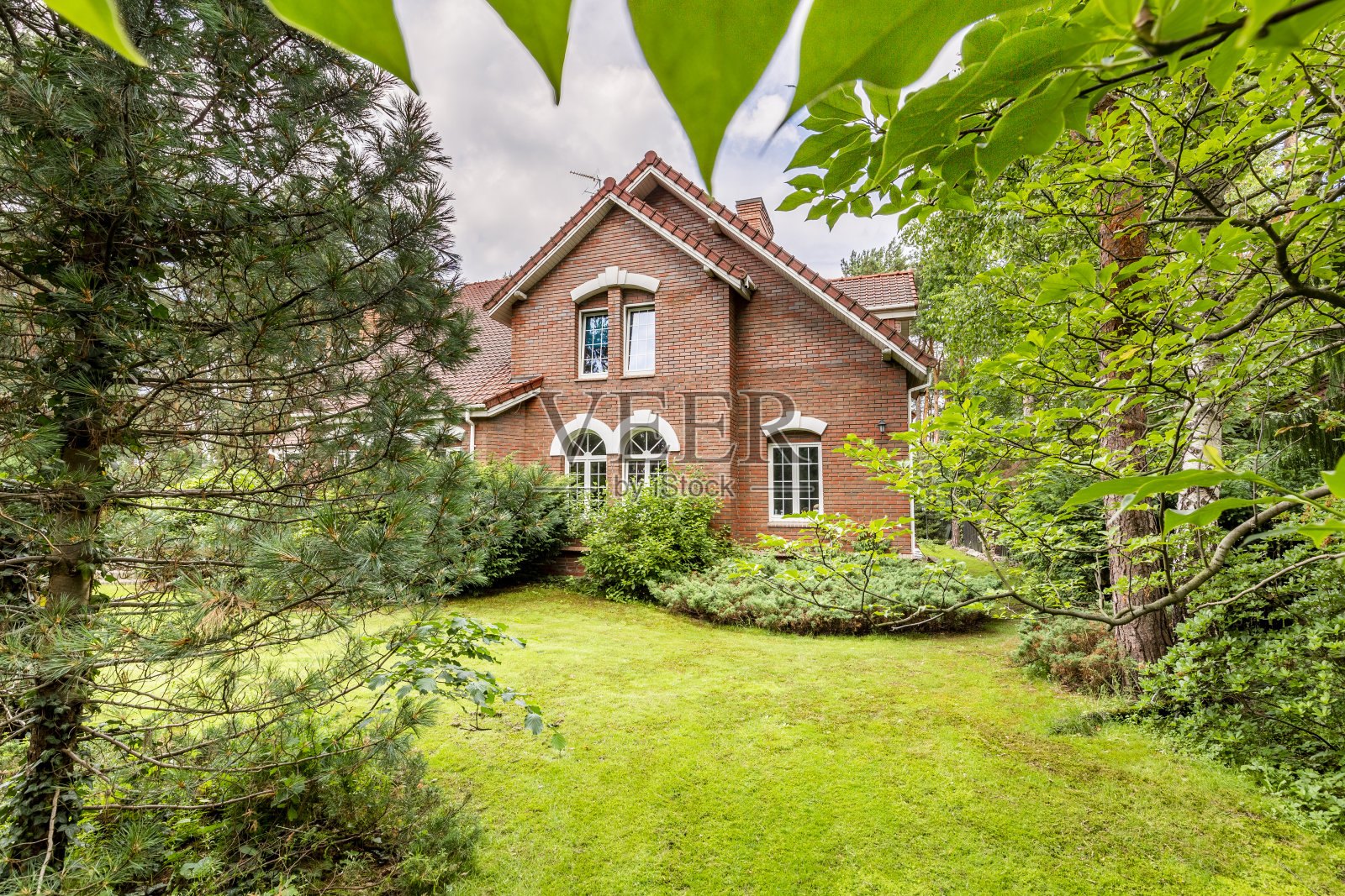 后院有绿色的草，树木和常青树的传统英国设计的乡村房子在红砖照片摄影图片