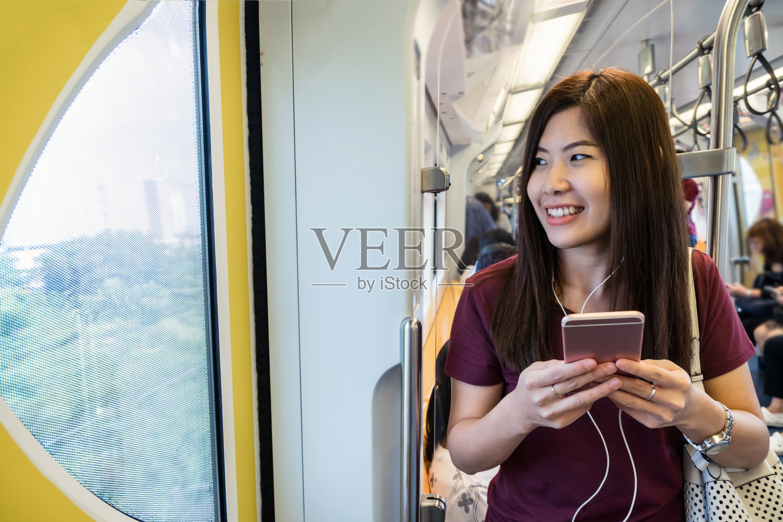 亚洲女性乘客与休闲套装使用智能手机在轻轨或地铁在大城市旅行，生活方式和交通理念照片摄影图片