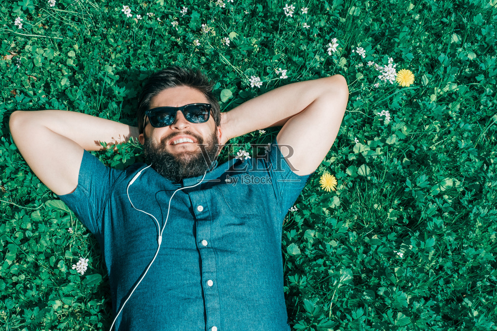 无忧无虑的男人戴着太阳镜躺在草地上听着春天的音乐照片摄影图片