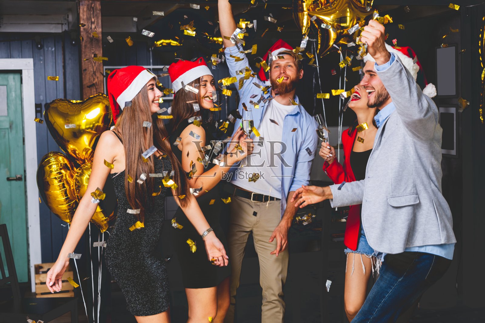 一起庆祝新年。一群美丽的年轻人戴着圣诞老人的帽子，投掷五颜六色的五彩纸屑，看起来很开心。照片摄影图片