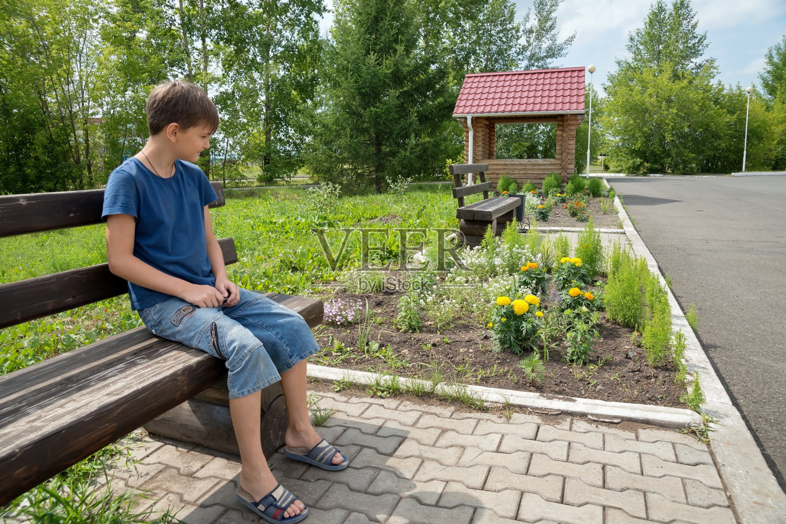 在一个阳光明媚的夏日，一个11岁的男孩坐在公园的木凳上沉思。照片摄影图片