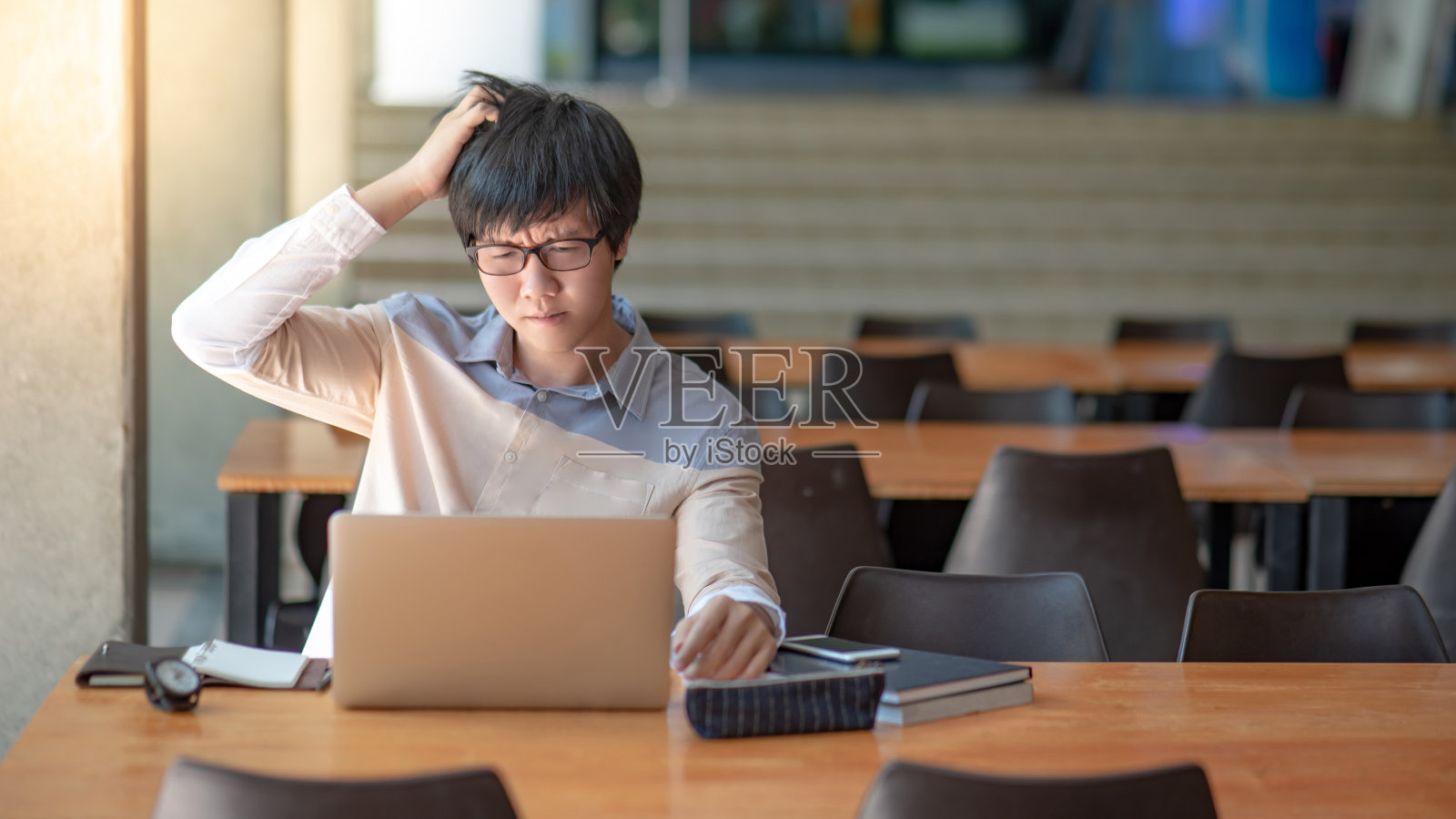 年轻的亚洲人大学学生戴着眼镜，在大学图书馆使用笔记本电脑时感到沮丧。教育建设中的校园生活方式。研究问题和解决方案的概念照片摄影图片