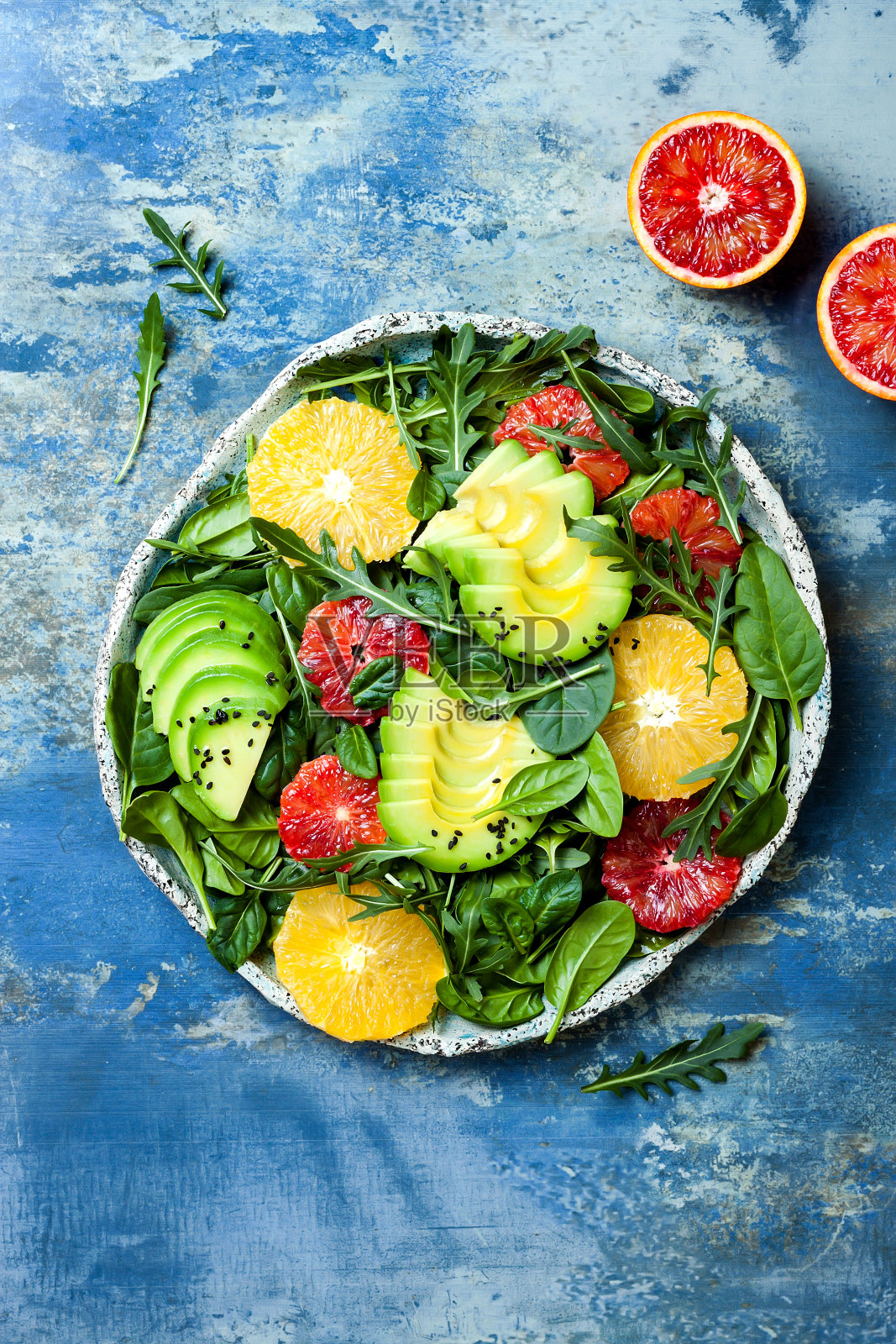 混合绿色蔬菜和血橙的柑橘沙拉。纯素、素食、清洁饮食、节食、饮食观念。蓝石头背景。照片摄影图片