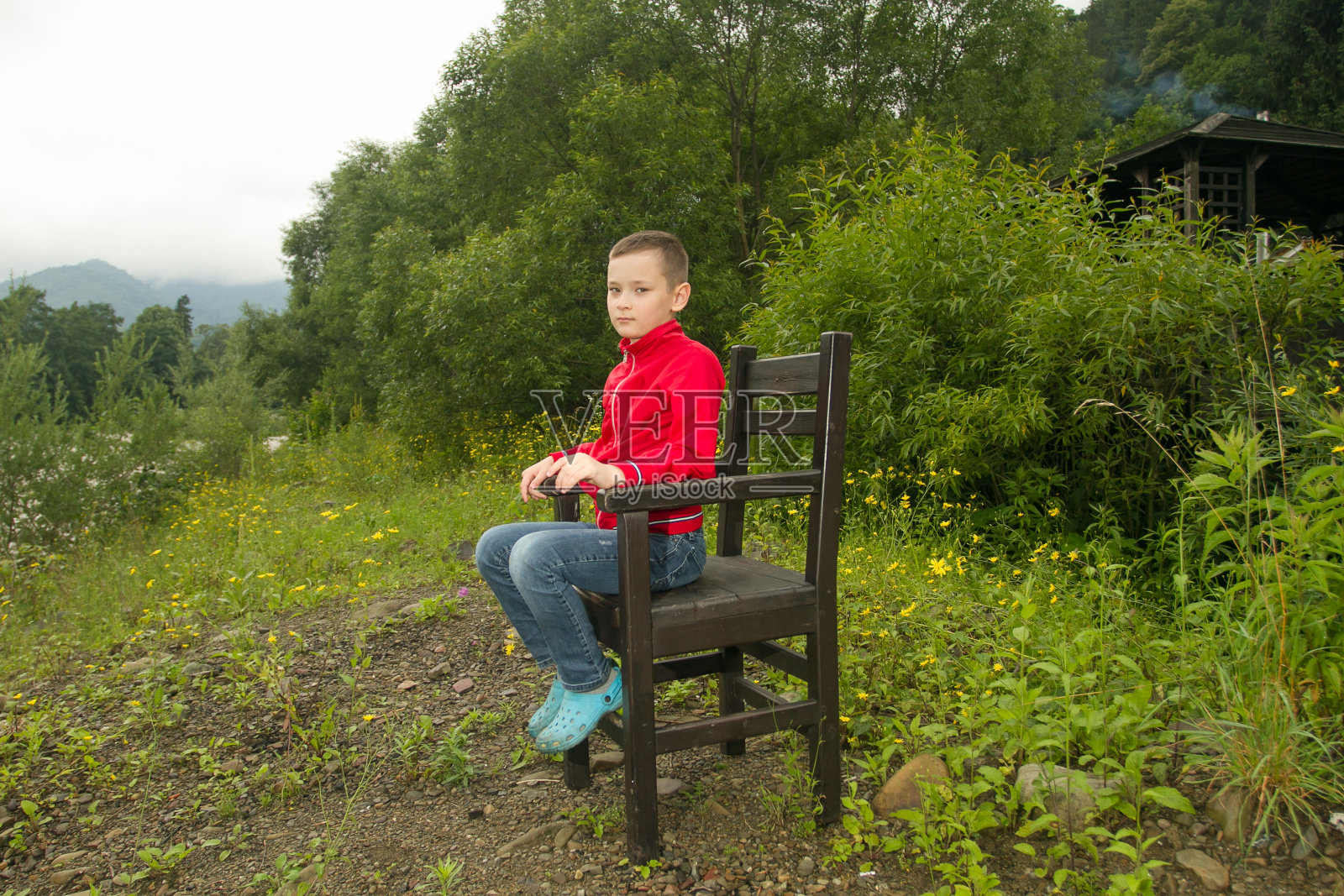 野生森林里坐在凳子或椅子上的男孩。孤独或悲伤的概念。悲伤的小男孩照片摄影图片