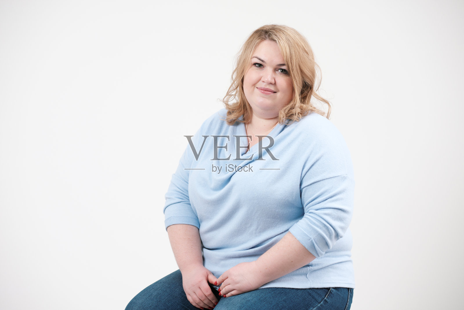在演播室里，白色背景下穿着休闲蓝色衣服的年轻肥胖妇女。Bodypositive。照片摄影图片
