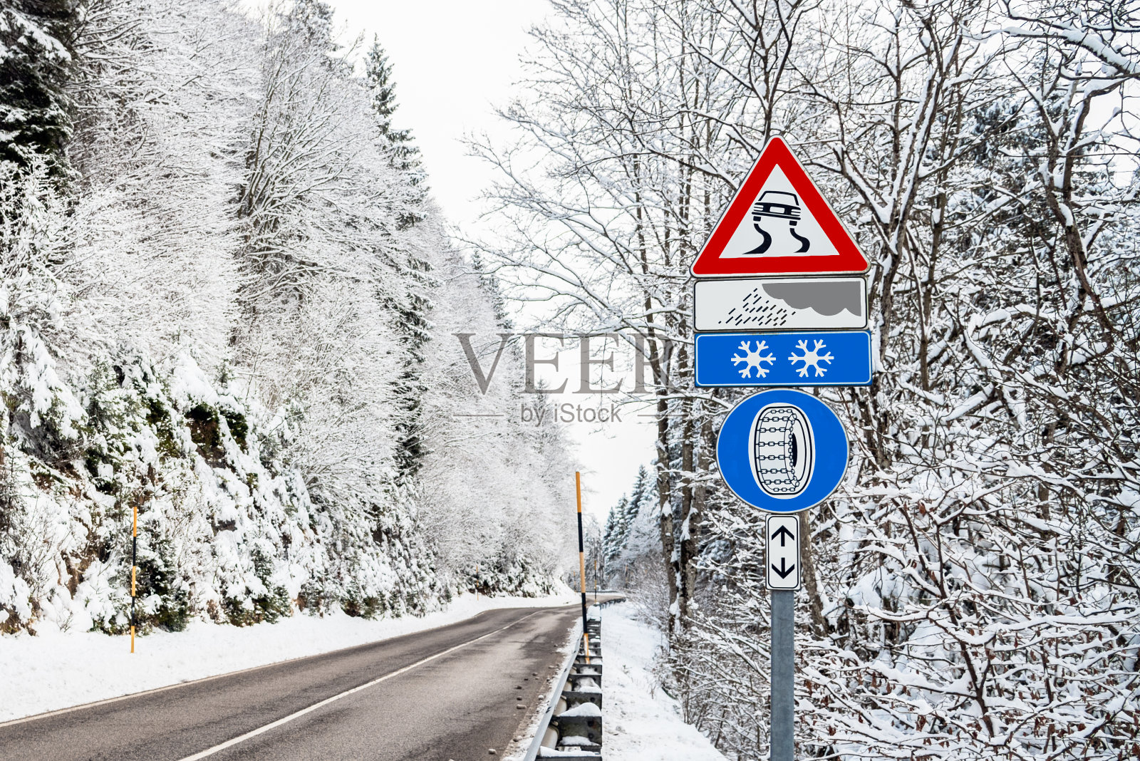 欧洲的三角形警告标志，在一个冬天的一天，通过一个被雪覆盖的森林的山路照片摄影图片