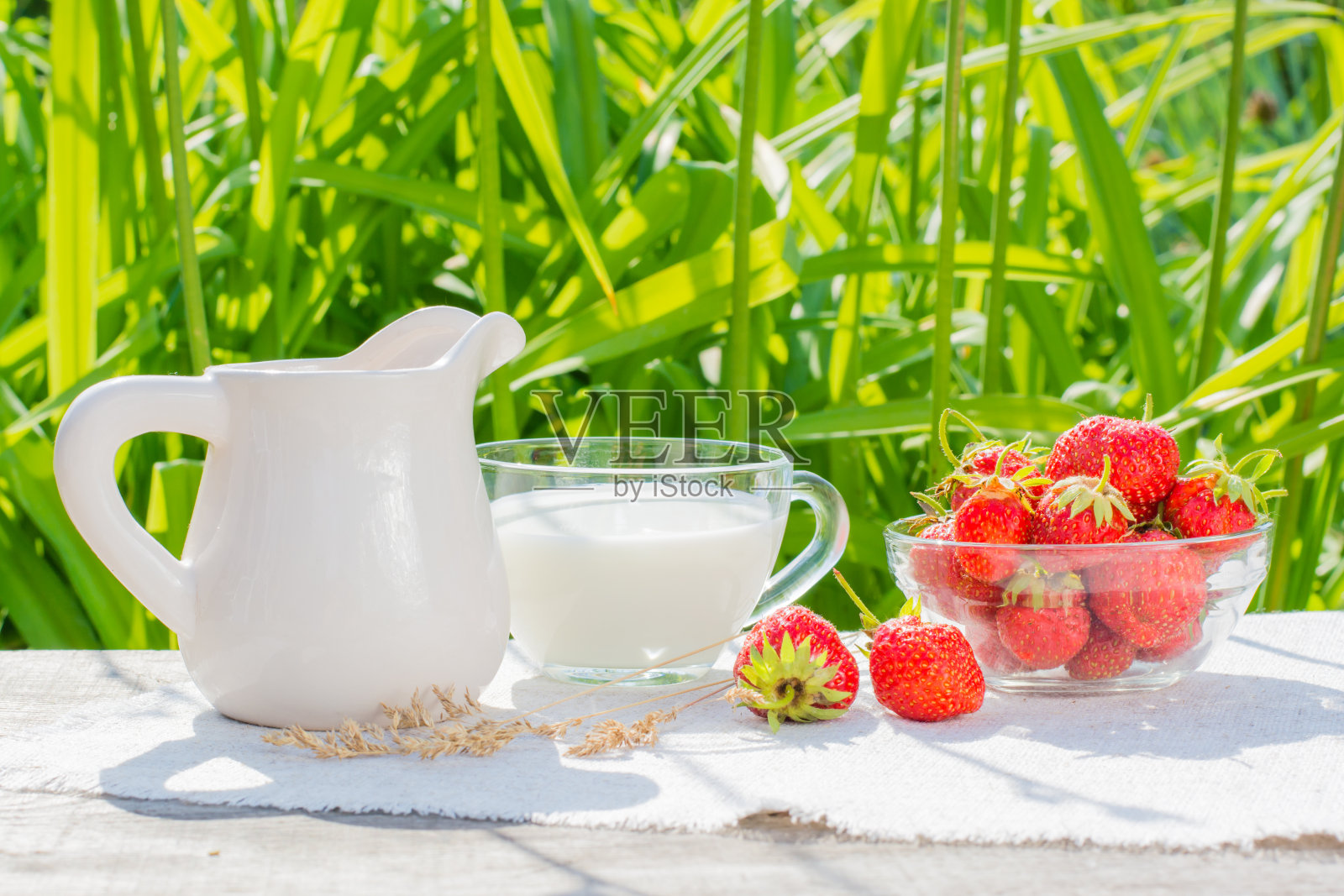 一碗草莓，一杯牛奶和一个水壶放在桌上的餐巾上照片摄影图片
