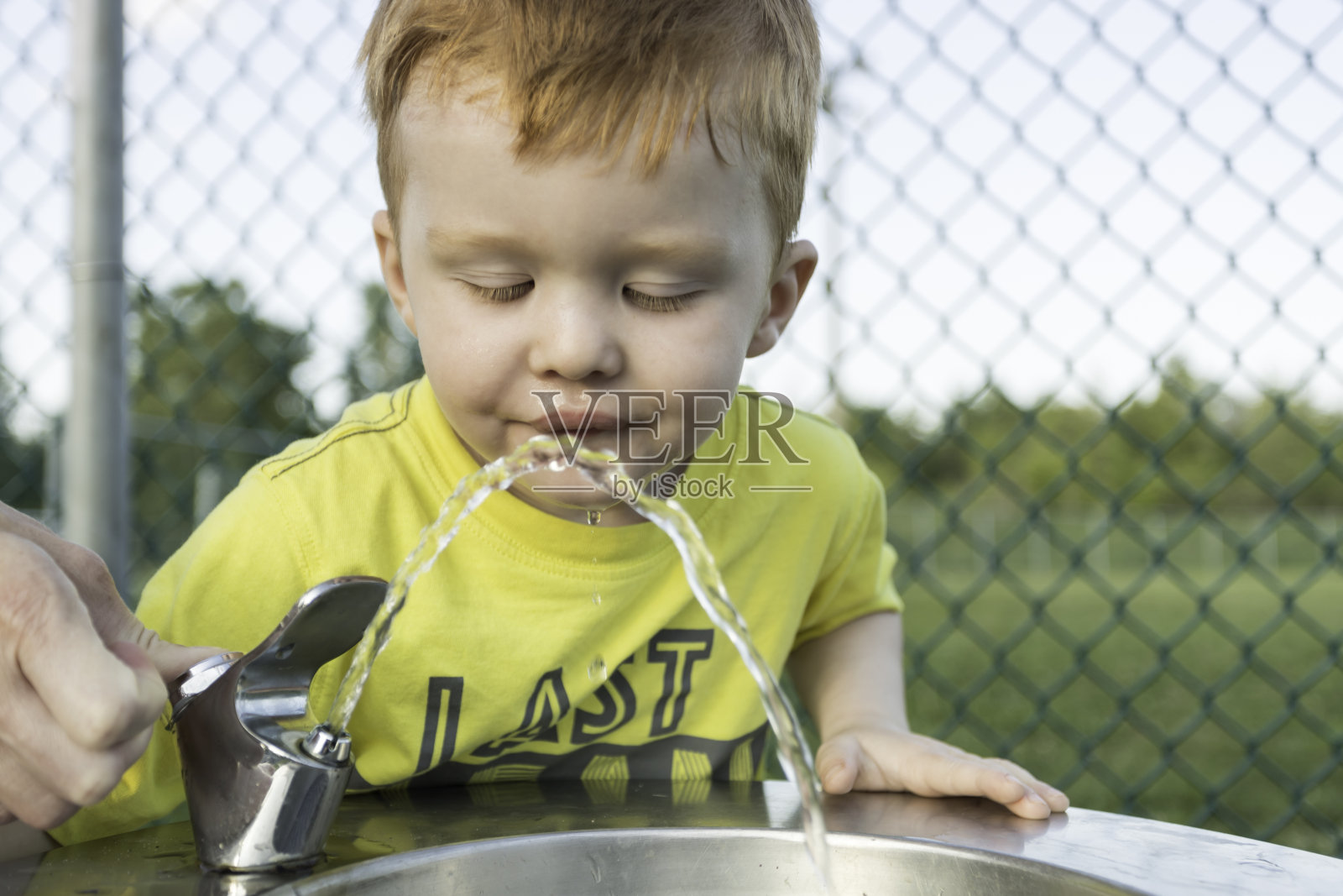 可爱的红发男孩从饮水机喝水照片摄影图片