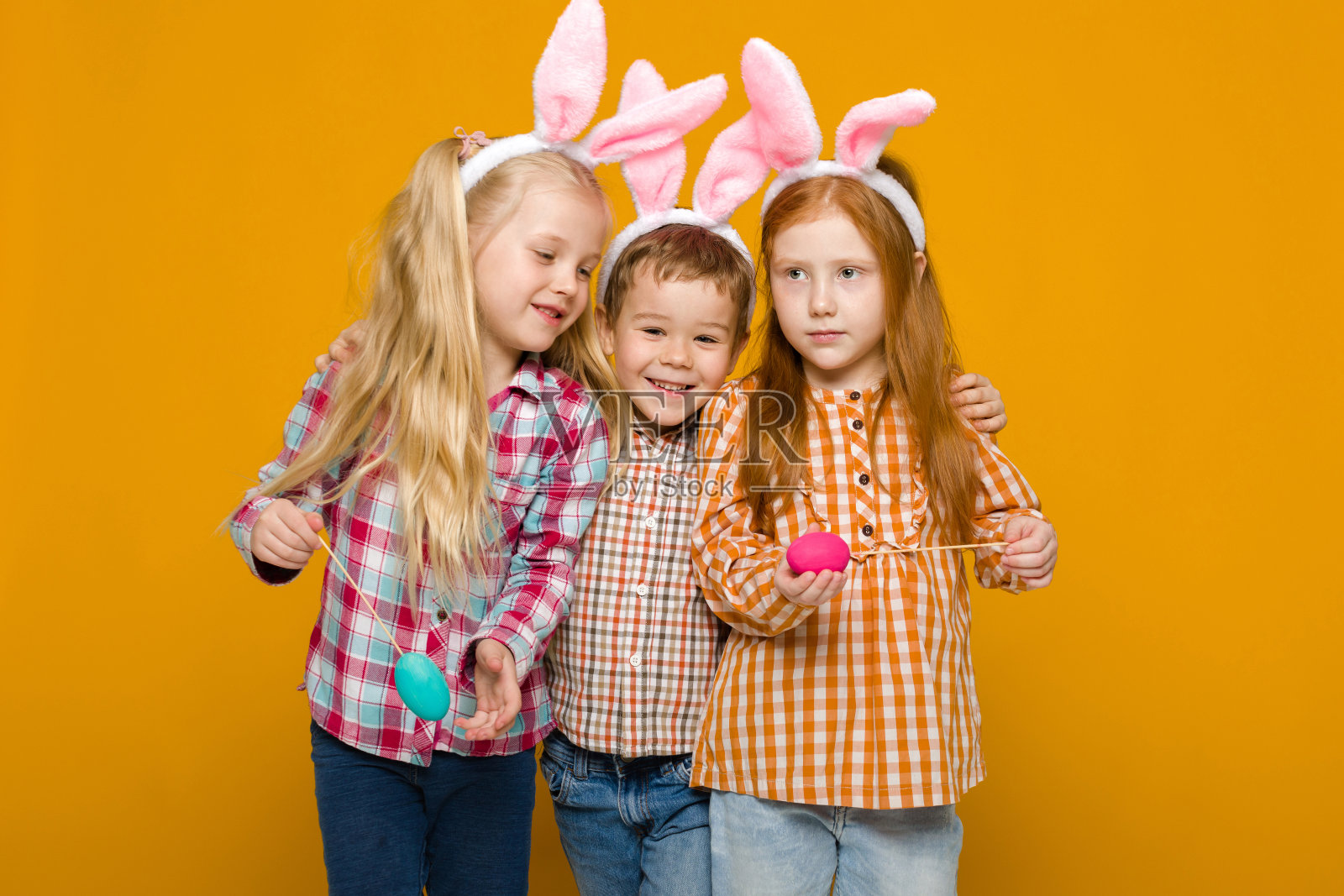 两个带着复活节兔子耳朵的小男孩和女孩，手里拿着五颜六色的彩蛋照片摄影图片