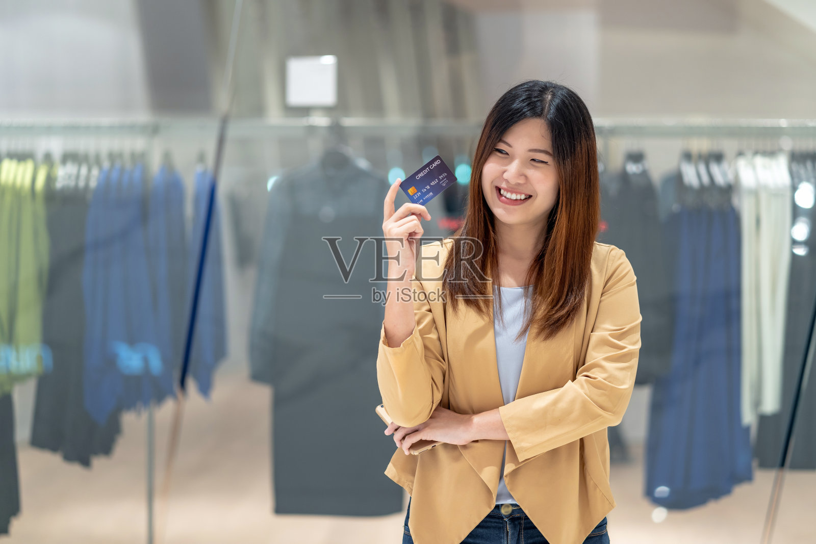 亚洲妇女使用信用卡与手机在百货商店网上购物的服装店背景，技术钱钱包和网上支付概念，信用卡模型照片摄影图片