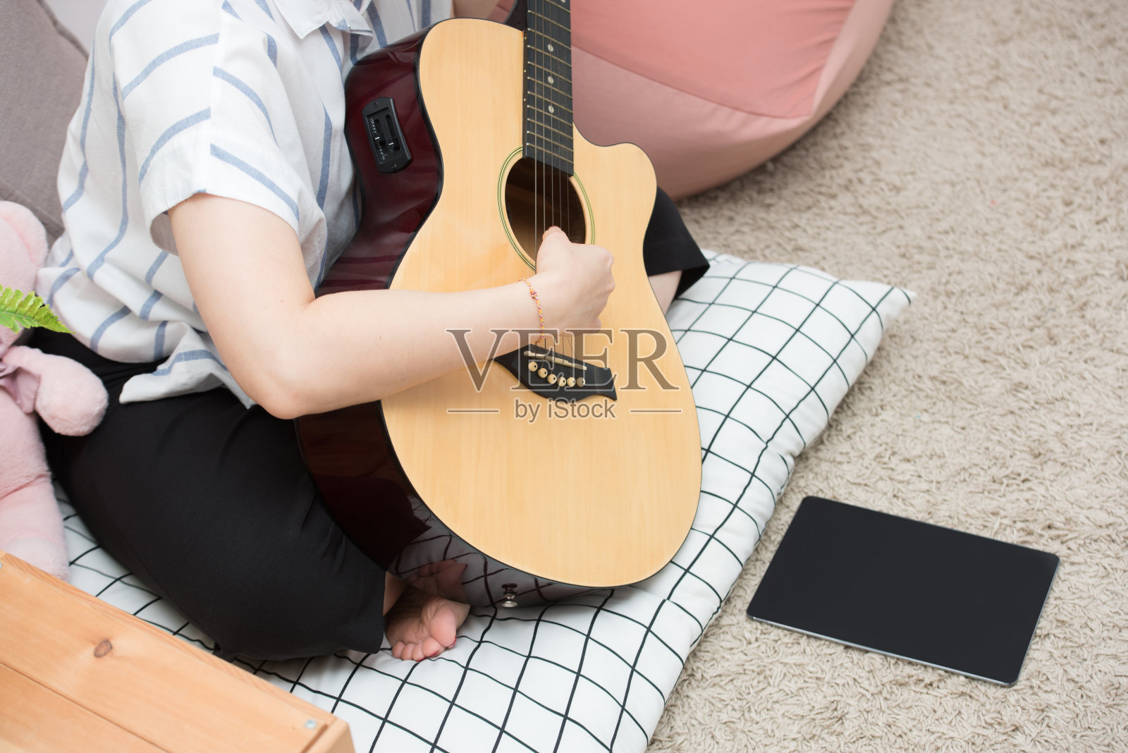 年轻的亚洲青少年黑发女孩长头发坐在地板上，在灰色的墙壁上弹奏黑色原声吉他照片摄影图片