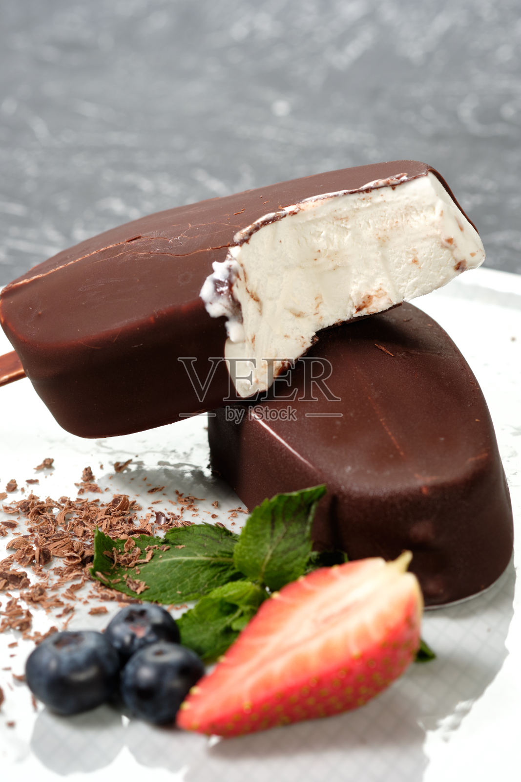 白色的盘子里放着巧克力奶油冰淇淋冰棒，上面有新鲜的夏季浆果，草莓，蓝莓照片摄影图片