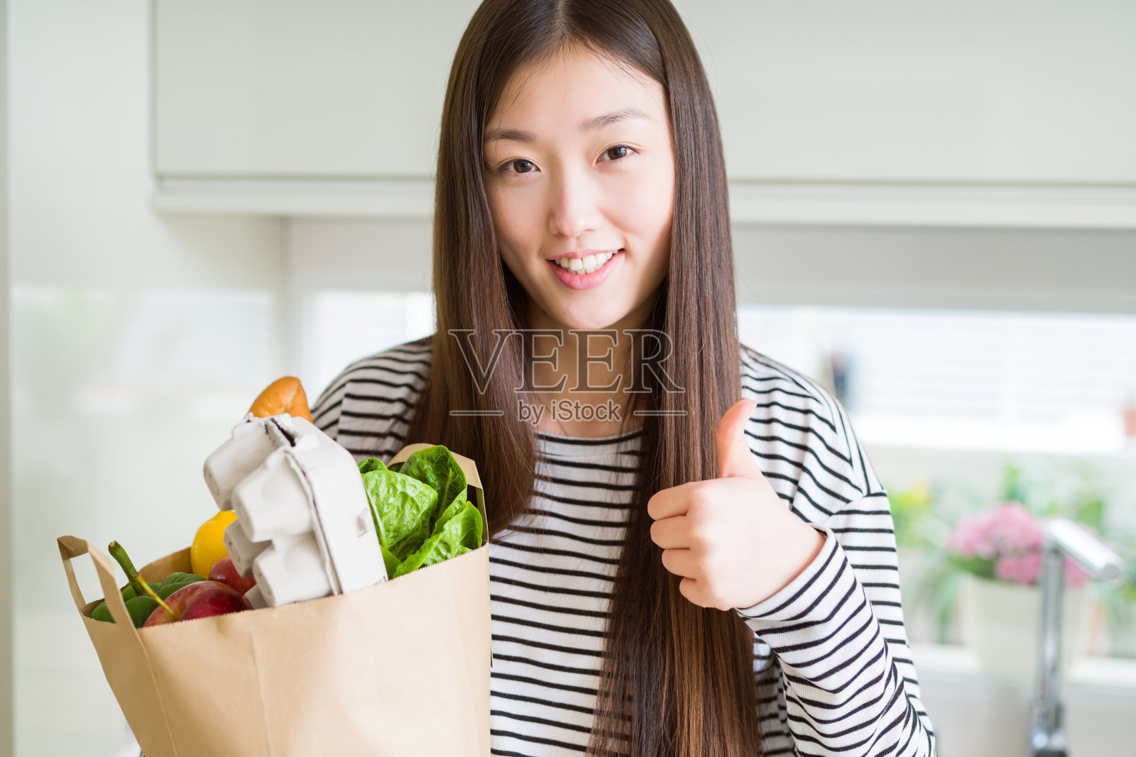 美丽的亚洲女人拿着纸袋新鲜的食品杂货与大微笑做ok的标志，拇指与手指，优秀的标志照片摄影图片