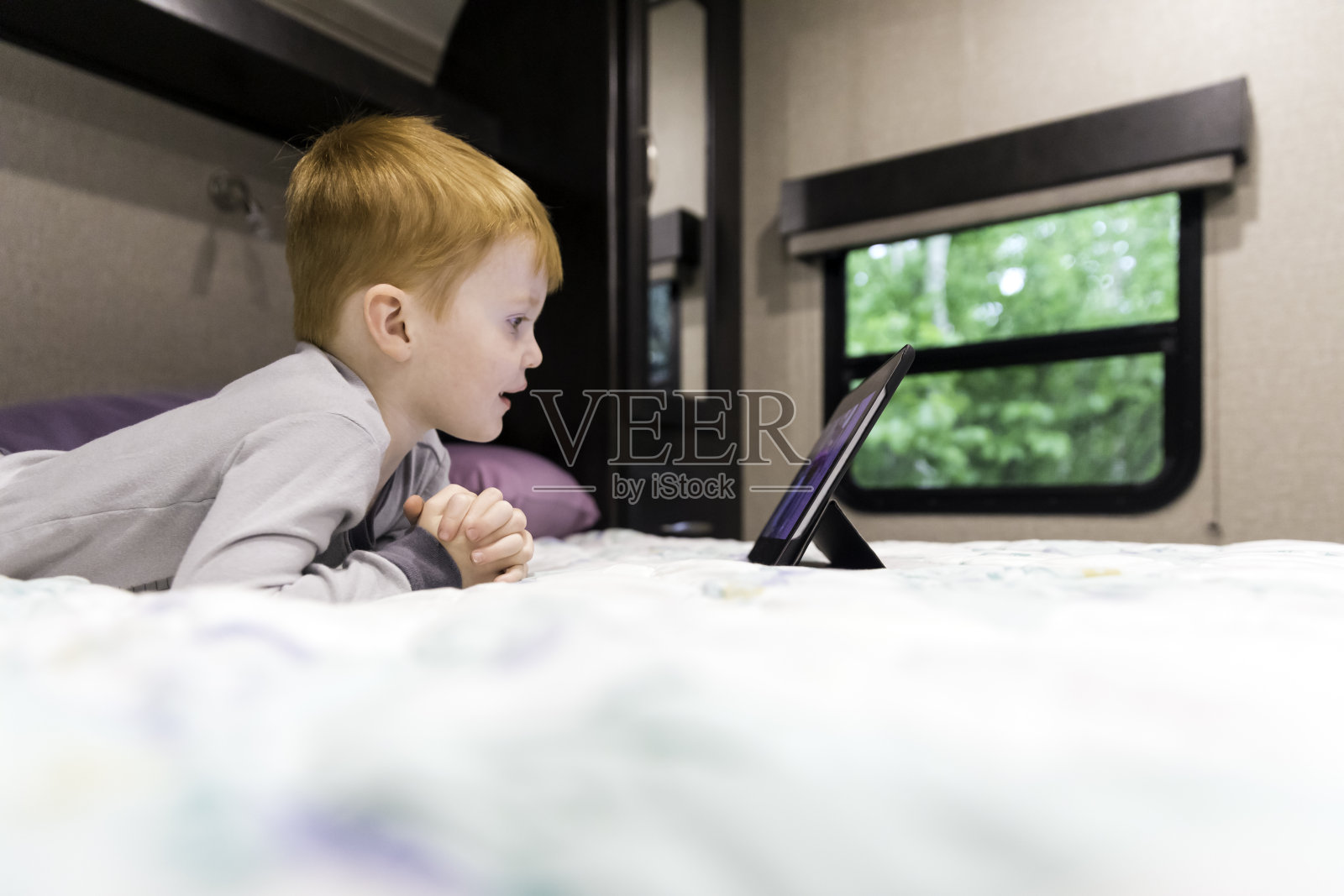 小红发男孩在露营拖车的数字平板电脑上看电视节目照片摄影图片