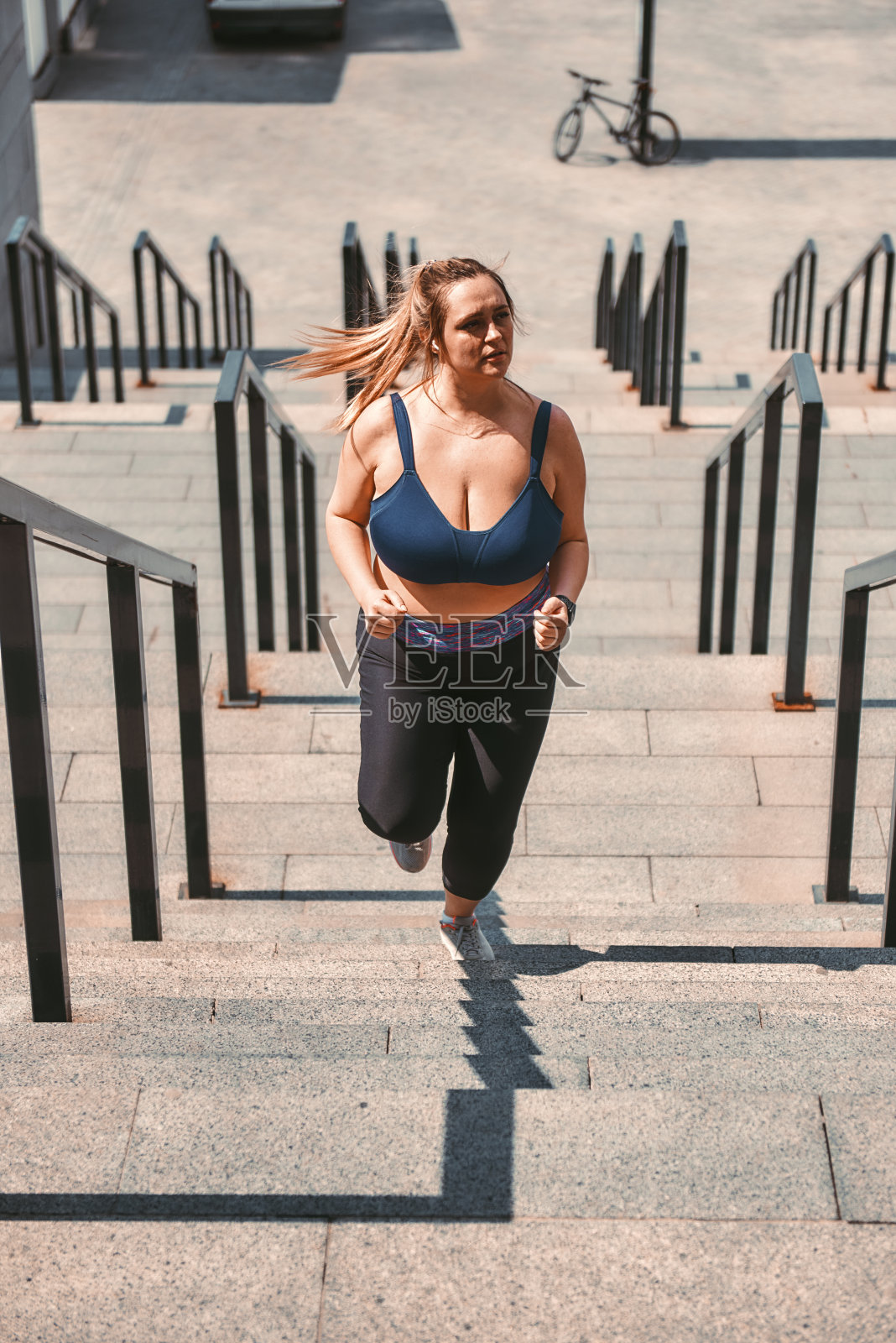 减肥。在户外运动时，穿着运动服跑上楼梯的漂亮大码女人照片摄影图片